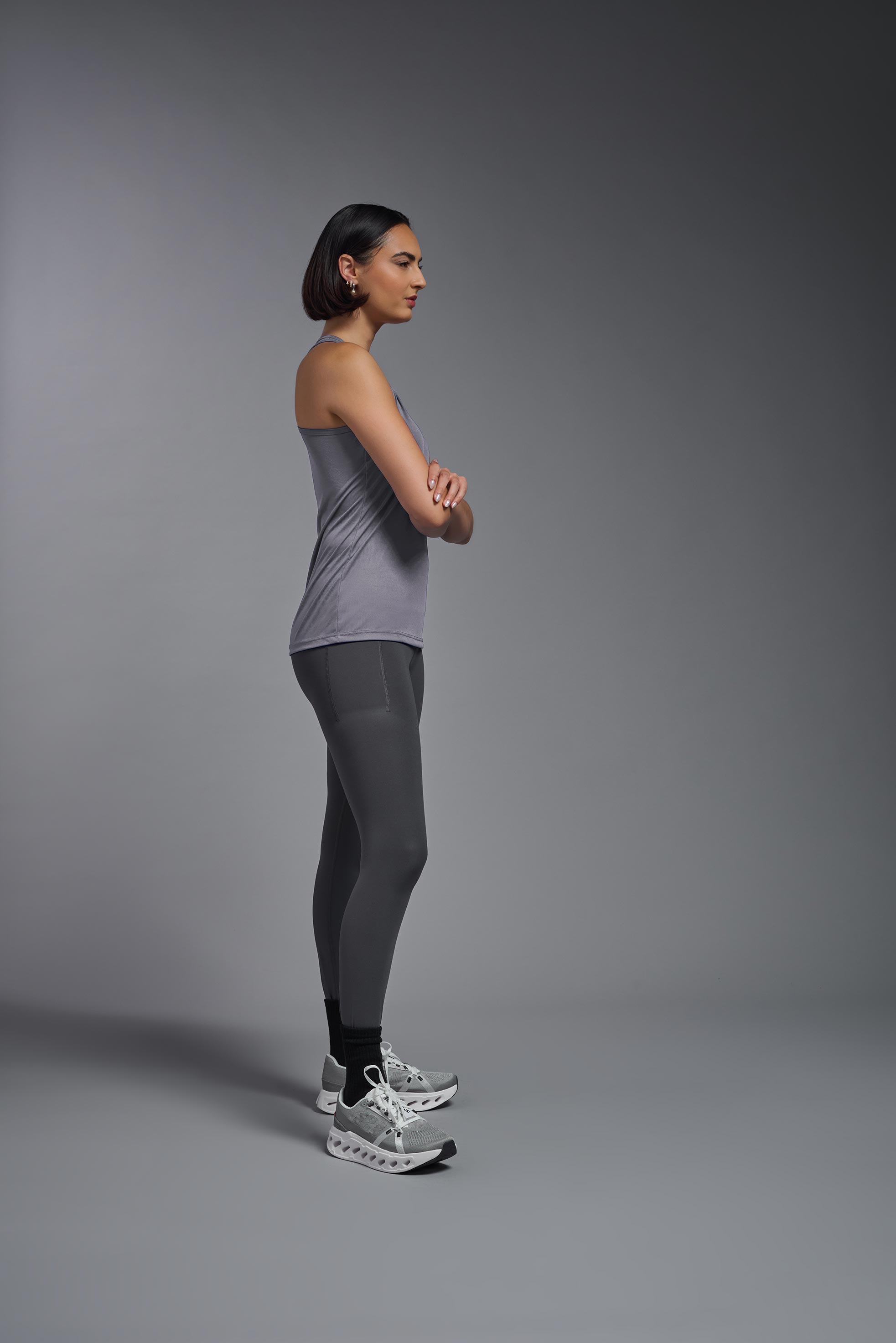 A female model wearing the women's DriMax Endurance Racerback Tank in the color steel gray, made out of 100% polyester, showing the relaxed fit from a side view. This tank is quick-drying, moisture-wicking, with up to 30 UV protection and made in the USA. #steel