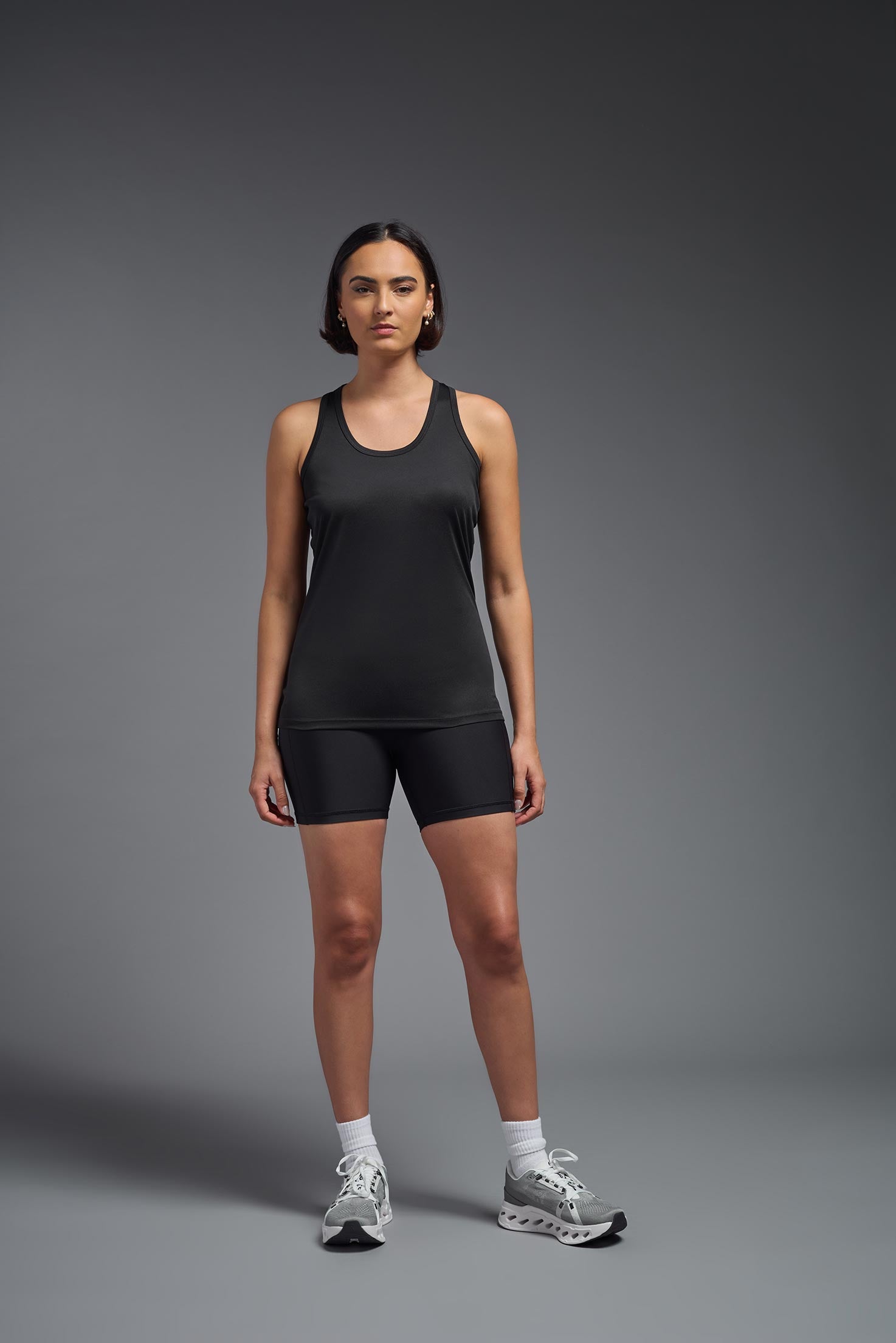 A female model wearing the women's DriMax Endurance Racerback Tank in the color black, made out of 100% polyester, showing the relaxed fit from a front view. This tank is quick-drying, moisture-wicking, with up to 30 UV protection and made in the USA. #black