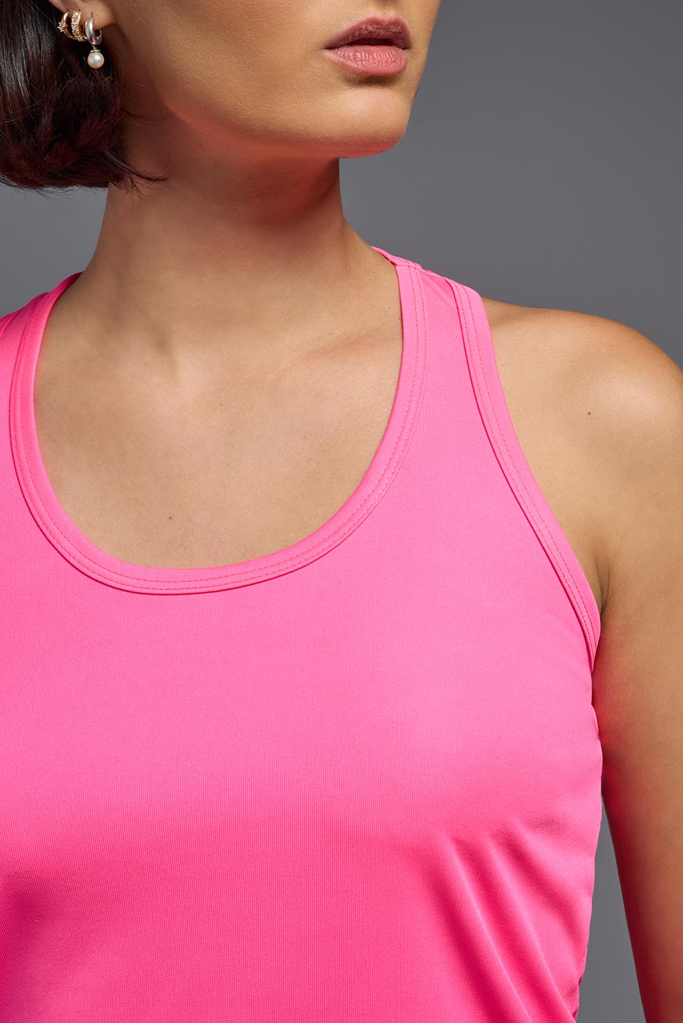 A female model wearing the women's DriMax Endurance Racerback Tank in the color hot pink, made out of 100% polyester, showing the relaxed fit from a close-up collar view. This tank is quick-drying, moisture-wicking, with up to 30 UV protection and made in the USA. #hot-pink