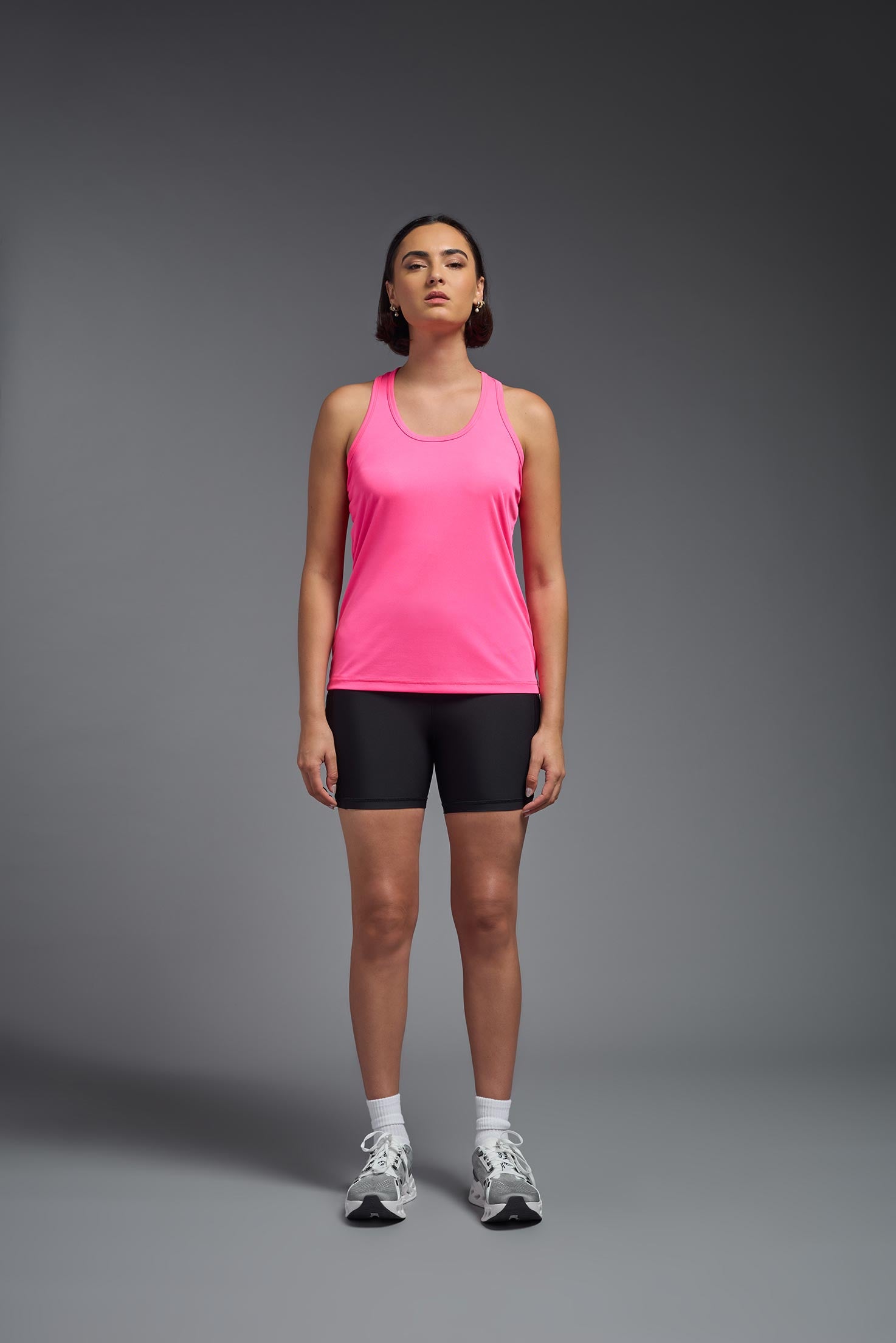 A female model wearing the women's DriMax Endurance Racerback Tank in the color hot pink, made out of 100% polyester, showing the relaxed fit from a front view. This tank is quick-drying, moisture-wicking, with up to 30 UV protection and made in the USA. #hot-pink