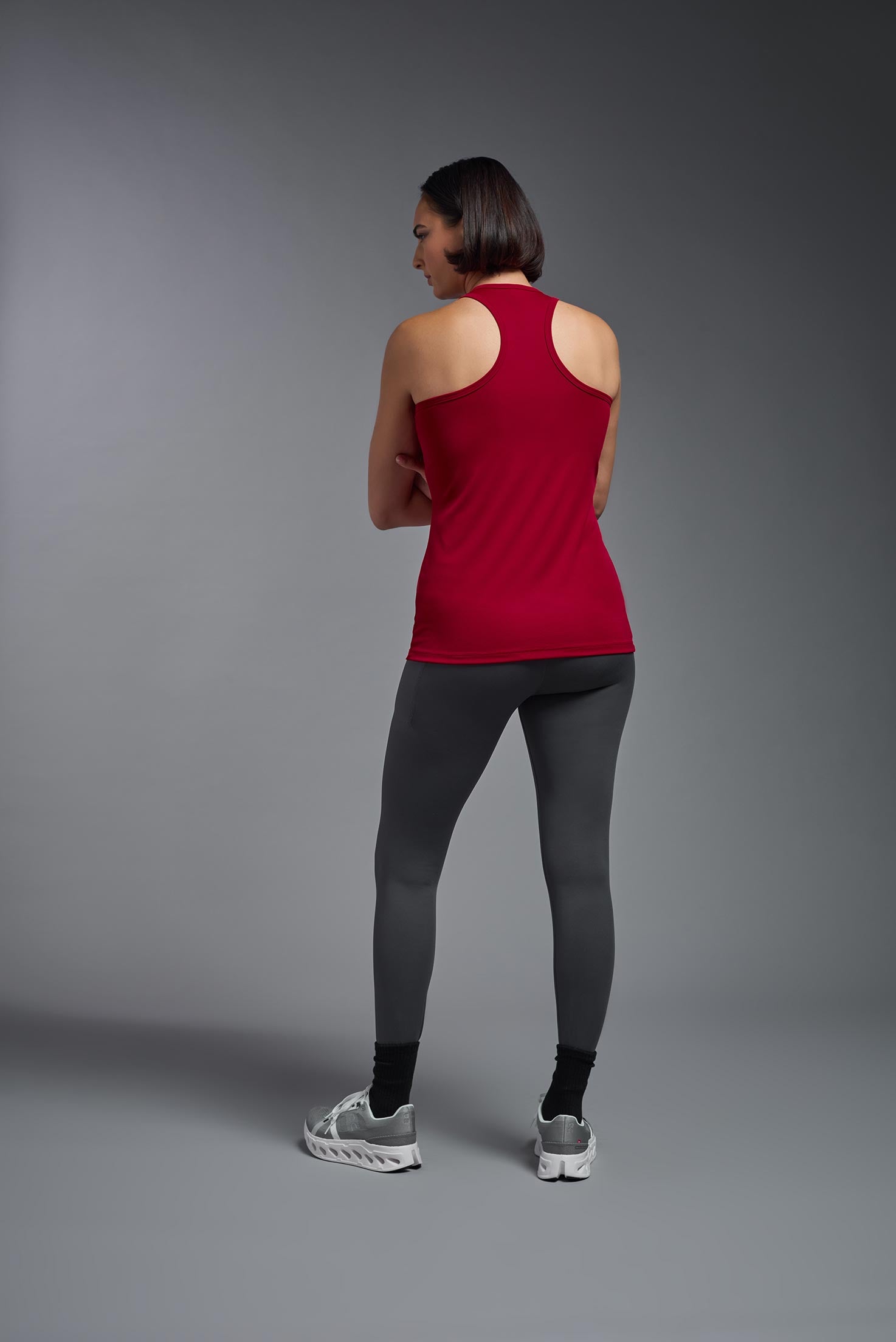 A female model wearing the women's DriMax Endurance Racerback Tank in the color red, made out of 100% polyester, showing the relaxed fit from a back view. This tank is quick-drying, moisture-wicking, with up to 30 UV protection and made in the USA. #red