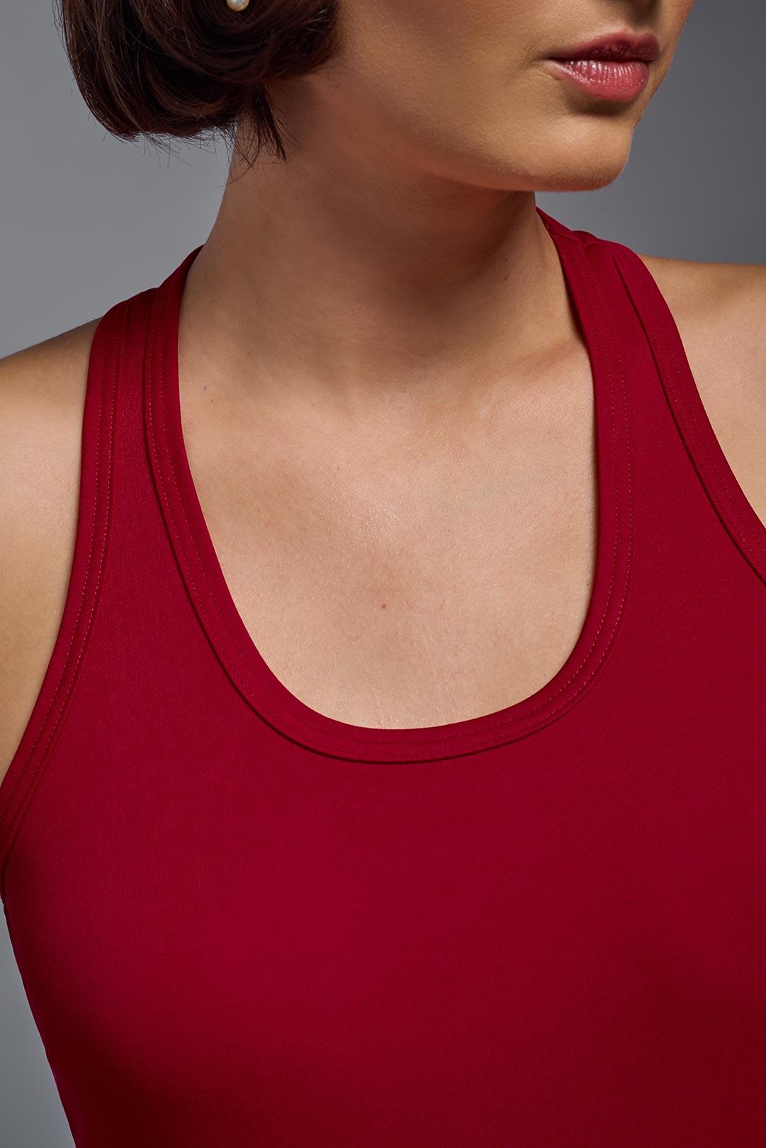 A female model wearing the women's DriMax Endurance Racerback Tank in the color red, made out of 100% polyester, showing the relaxed fit from a collar close-up view. This tank is quick-drying, moisture-wicking, with up to 30 UV protection and made in the USA. #hot-pink