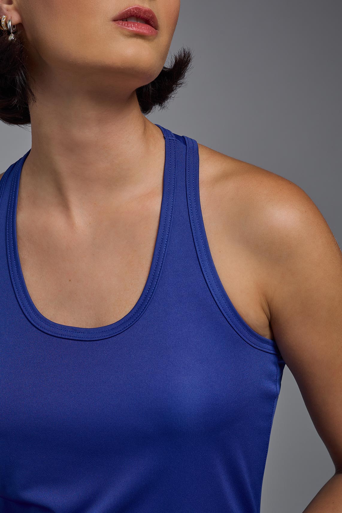 A female model wearing the women's DriMax Endurance Racerback Tank in the color royal blue, made out of 100% polyester, showing the relaxed fit from a close-up collar view. This tank is quick-drying, moisture-wicking, with up to 30 UV protection and made in the USA. #royal