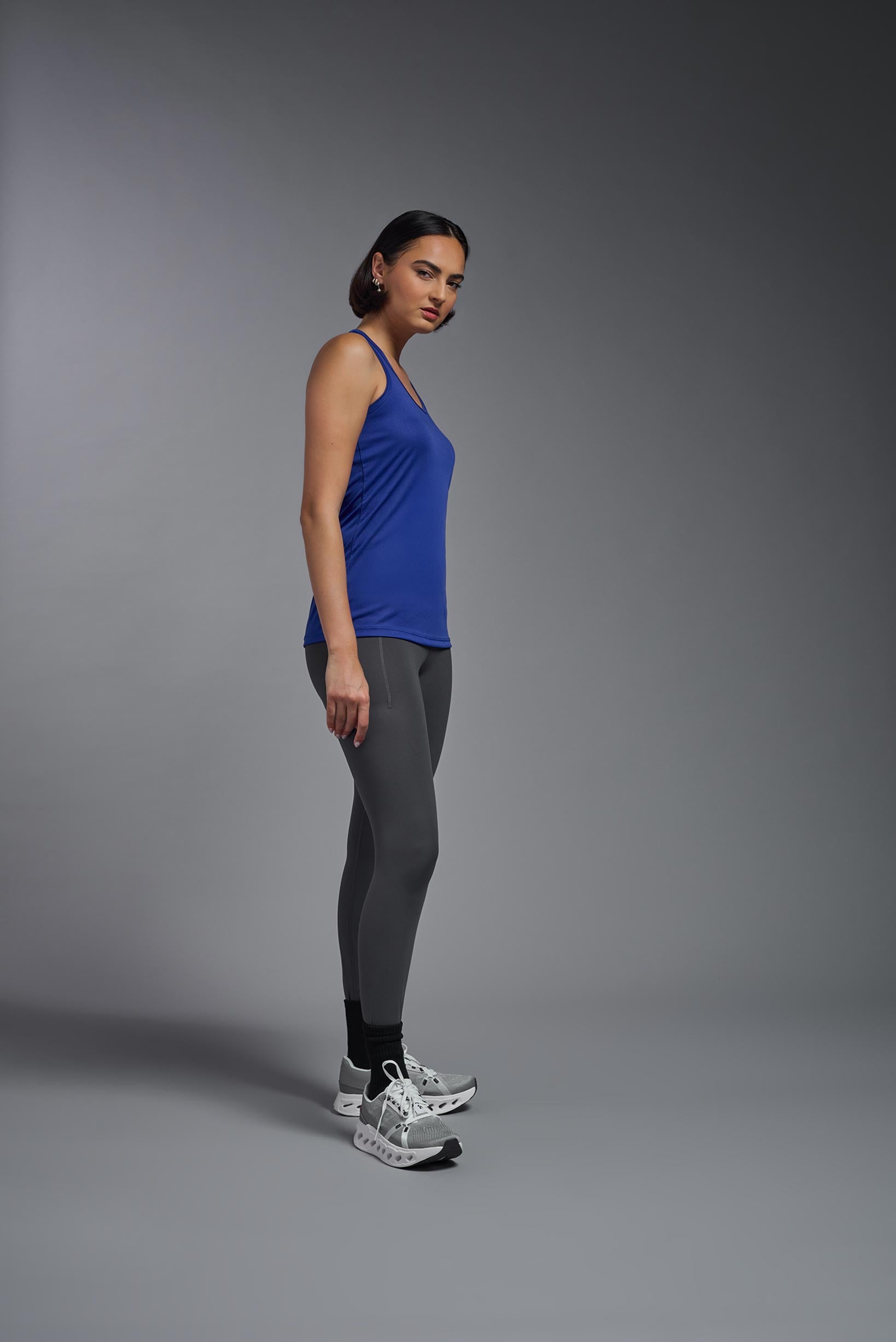 A female model wearing the women's DriMax Endurance Racerback Tank in the color royal blue, made out of 100% polyester, showing the relaxed fit from a side view. This tank is quick-drying, moisture-wicking, with up to 30 UV protection and made in the USA. #royal