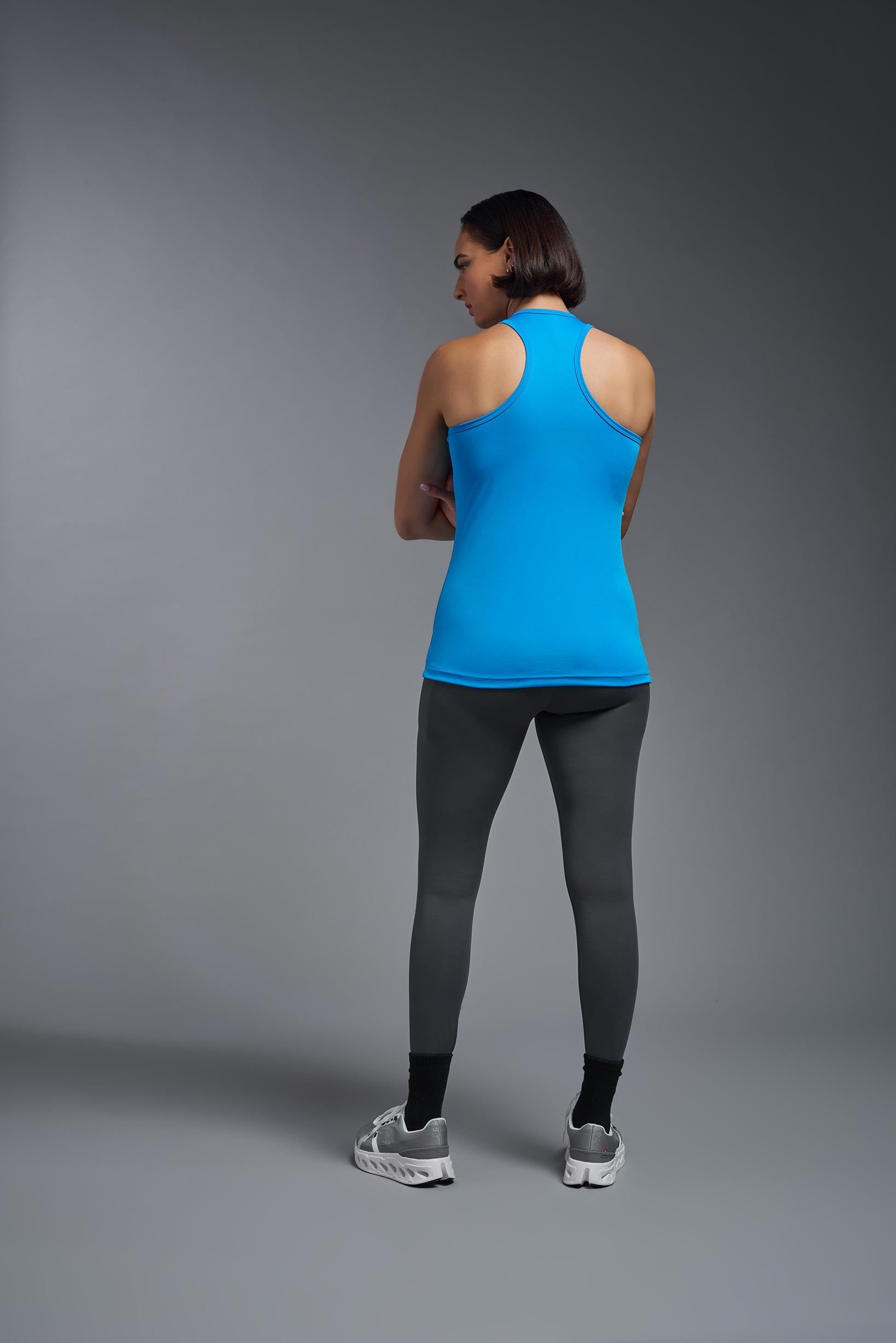 A female model wearing the women's DriMax Endurance Racerback Tank in the color safety blue, made out of 100% polyester, showing the relaxed fit from a back view. This tank is quick-drying, moisture-wicking, with up to 30 UV protection and made in the USA. #safety-blue