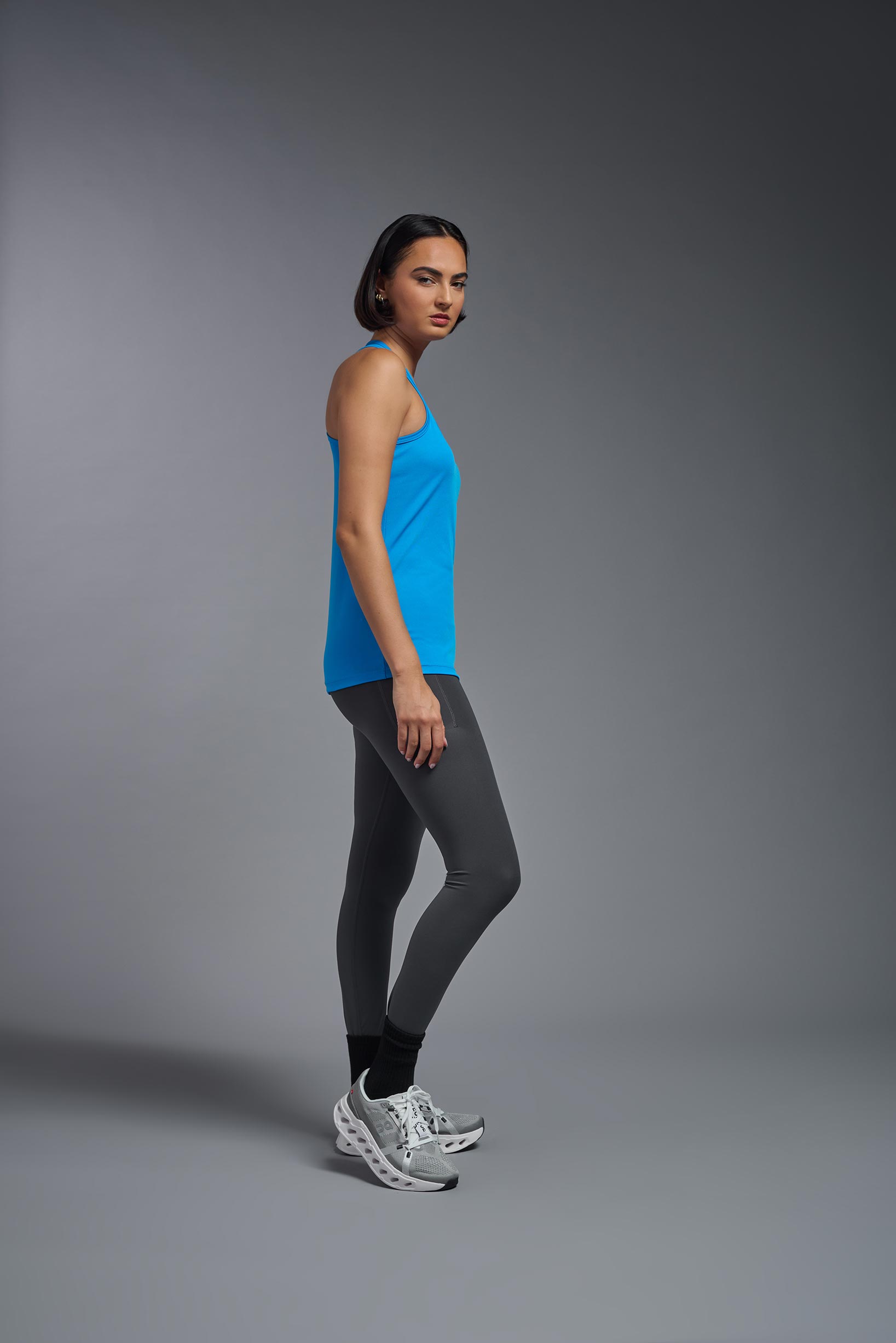 A female model wearing the women's DriMax Endurance Racerback Tank in the color safety blue, made out of 100% polyester, showing the relaxed fit from a side view. This tank is quick-drying, moisture-wicking, with up to 30 UV protection and made in the USA. #safety-blue