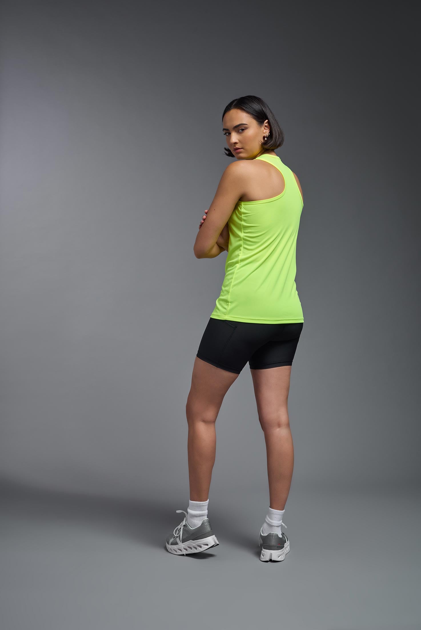 A female model wearing the women's DriMax Endurance Racerback Tank in the color safety yellow, made out of 100% polyester, showing the relaxed fit from a side view. This tank is quick-drying, moisture-wicking, with up to 30 UV protection and made in the USA. #safety-yellow