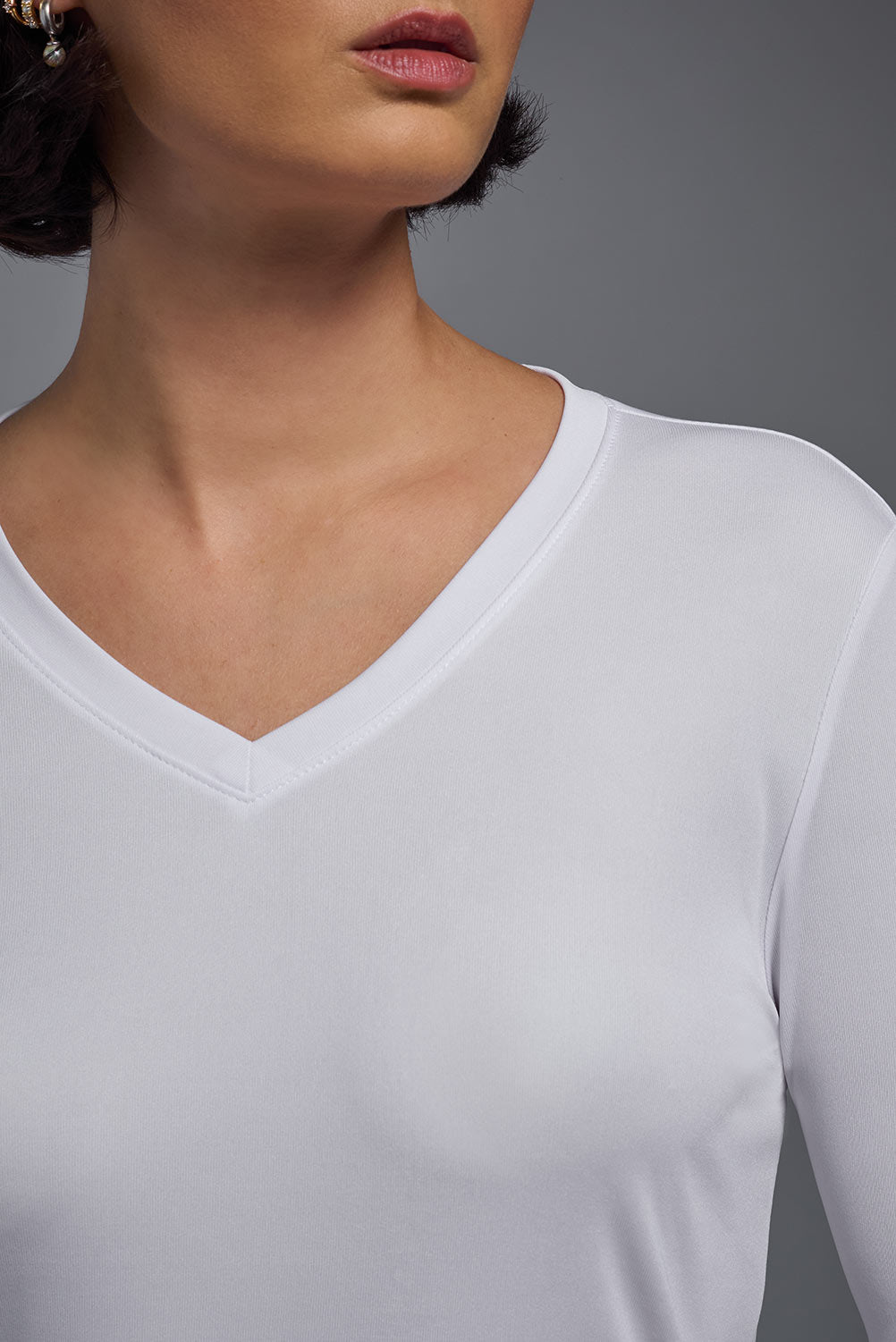 A female model wearing the women's DriMax V-Neck Long Sleeve Expert Tee  in the color white, made out of 100% polyester, showing the relaxed fit from a close-up collar view. This shirt is quick-drying, moisture-wicking, with up to 30 UV protection and made in the USA. #white