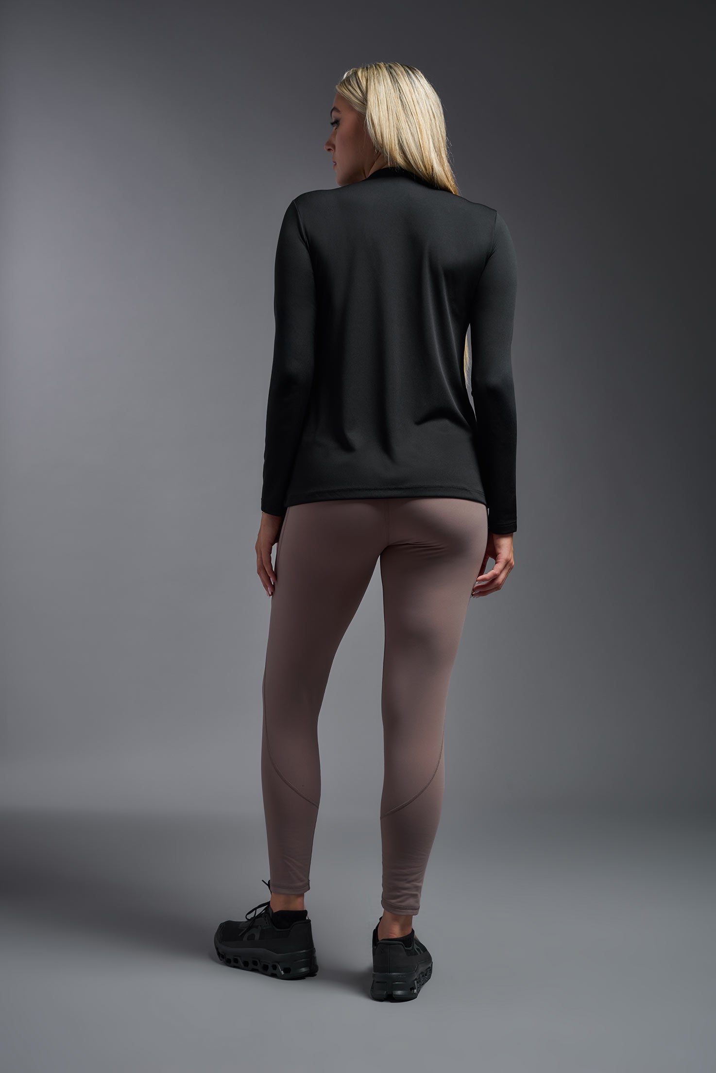 A female model wearing the women's DriMax V-Neck Long Sleeve Expert Tee  in the color black, made out of 100% polyester, showing the relaxed fit from a back view. This shirt is quick-drying, moisture-wicking, with up to 30 UV protection and made in the USA. #black