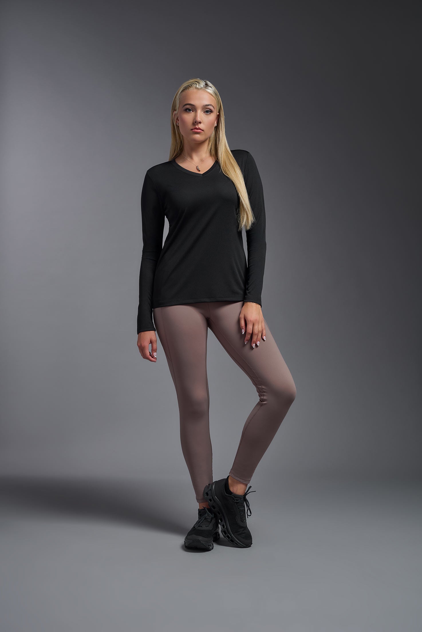 A female model wearing the women's DriMax V-Neck Long Sleeve Expert Tee  in the color black, made out of 100% polyester, showing the relaxed fit from a front view. This shirt is quick-drying, moisture-wicking, with up to 30 UV protection and made in the USA. #black