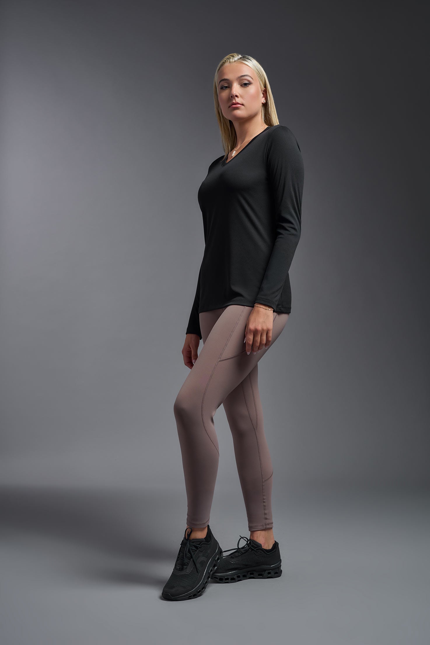 A female model wearing the women's DriMax V-Neck Long Sleeve Expert Tee  in the color black, made out of 100% polyester, showing the relaxed fit from a side view. This shirt is quick-drying, moisture-wicking, with up to 30 UV protection and made in the USA. #black