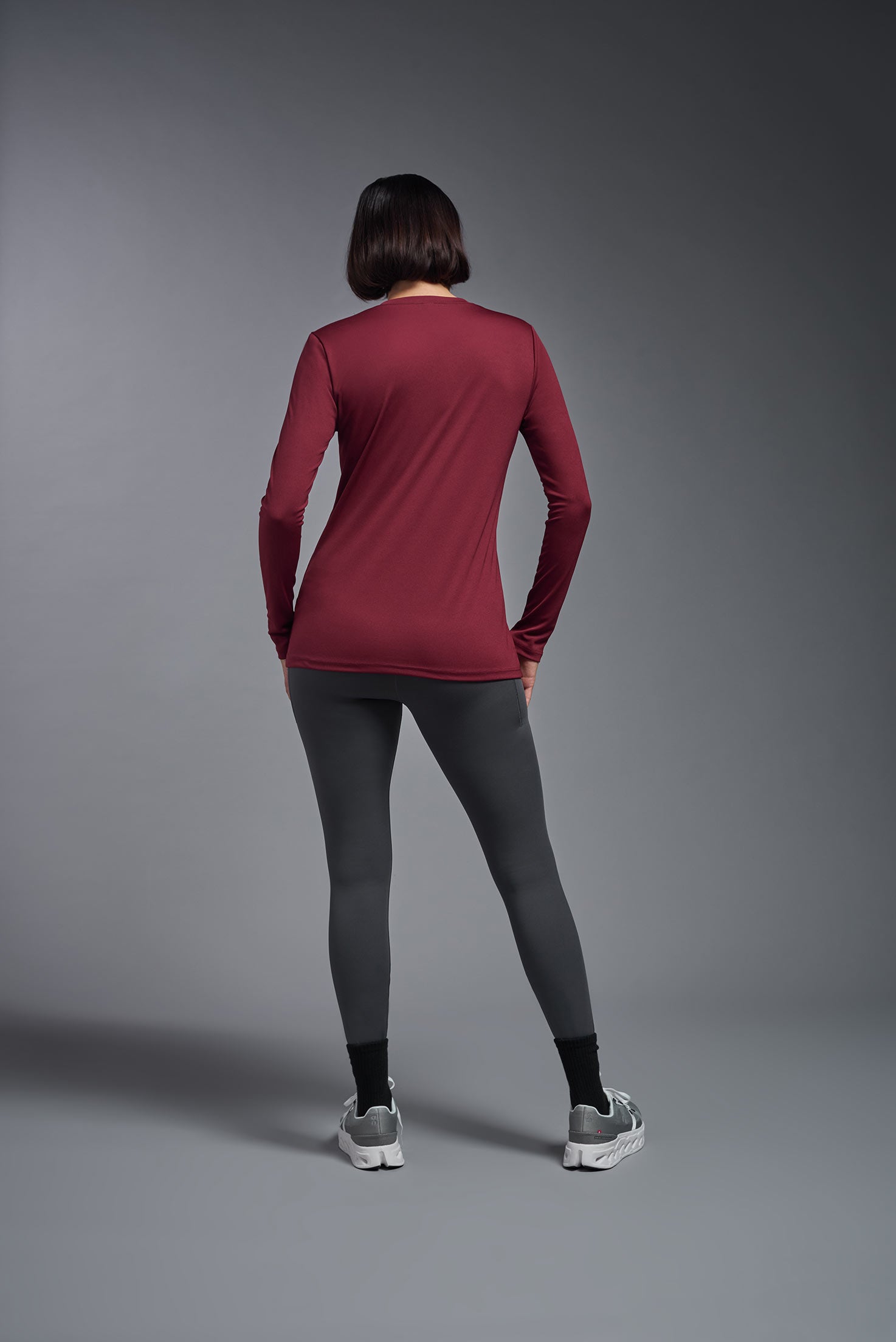 A female model wearing the women's DriMax V-Neck Long Sleeve Expert Tee  in the color cardinal, made out of 100% polyester, showing the relaxed fit from a back view. This shirt is quick-drying, moisture-wicking, with up to 30 UV protection and made in the USA. #cardinal