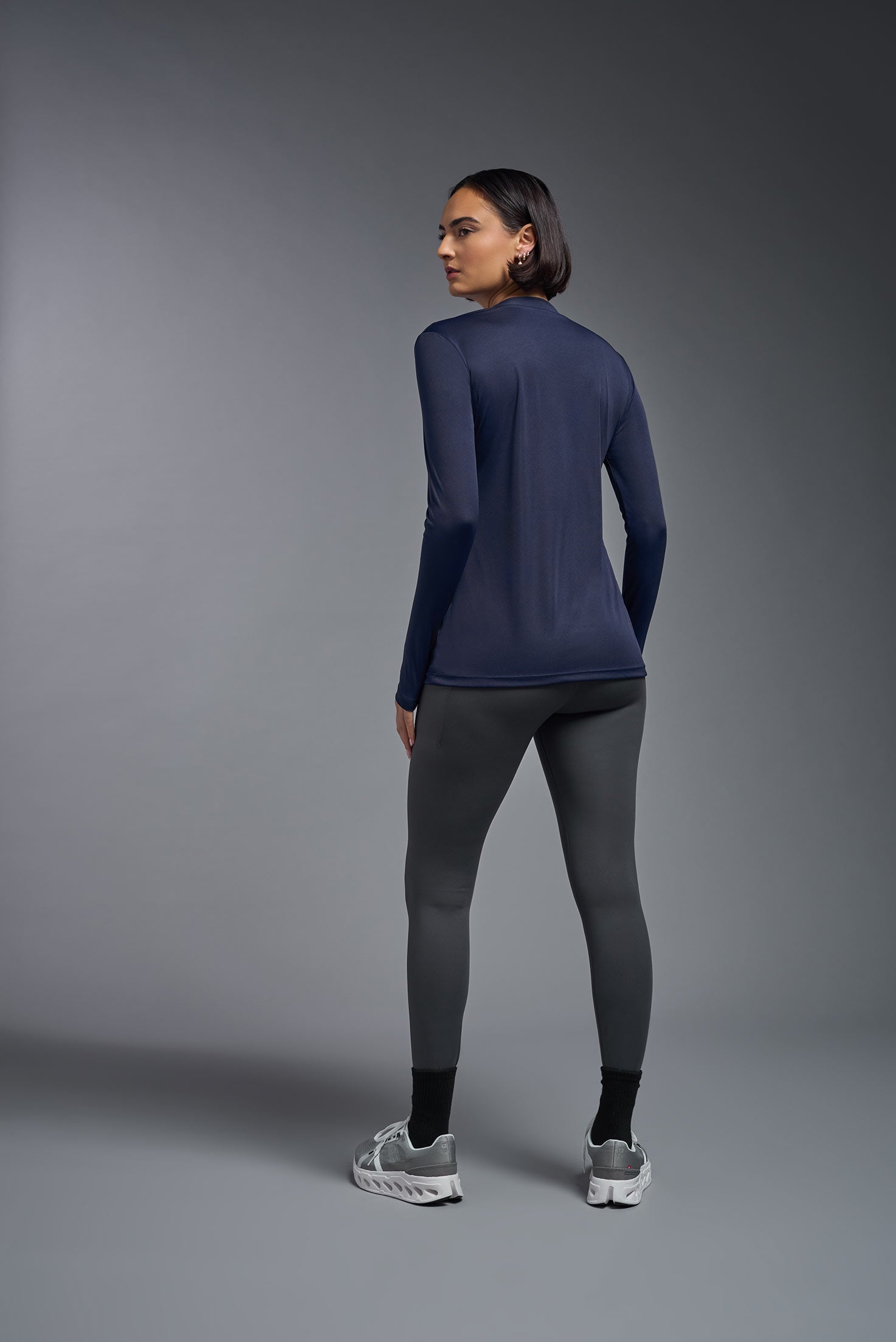 A female model wearing the women's DriMax V-Neck Long Sleeve Expert Tee  in the color navy, made out of 100% polyester, showing the relaxed fit from a back view. This shirt is quick-drying, moisture-wicking, with up to 30 UV protection and made in the USA. #navy