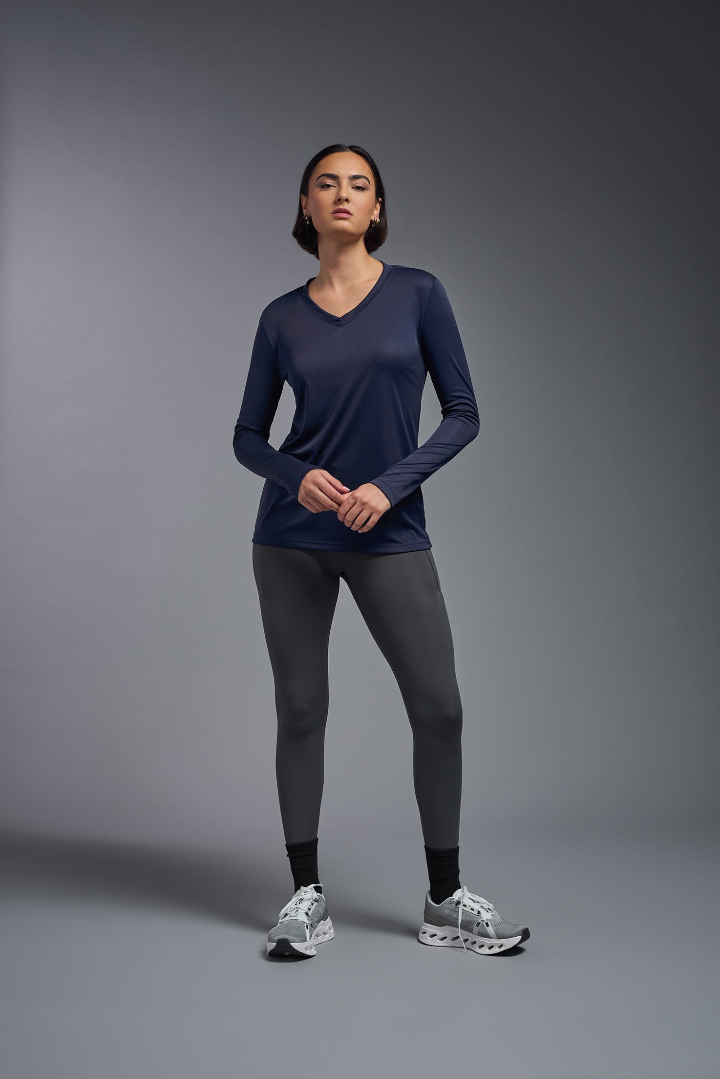 A female model wearing the women's DriMax V-Neck Long Sleeve Expert Tee  in the color navy, made out of 100% polyester, showing the relaxed fit from a front view. This shirt is quick-drying, moisture-wicking, with up to 30 UV protection and made in the USA. #navy