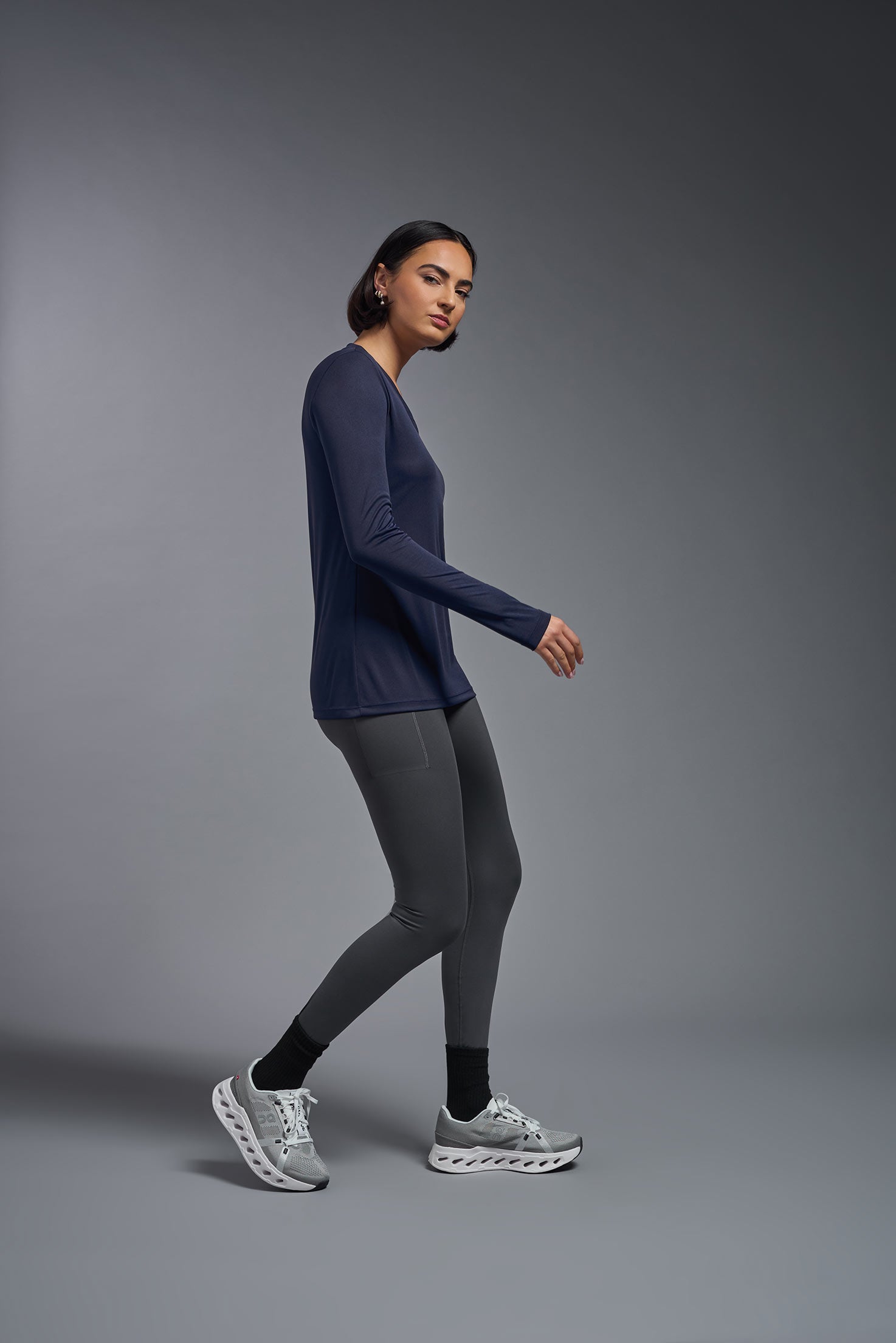 A female model wearing the women's DriMax V-Neck Long Sleeve Expert Tee  in the color navy, made out of 100% polyester, showing the relaxed fit from a side view. This shirt is quick-drying, moisture-wicking, with up to 30 UV protection and made in the USA. #navy