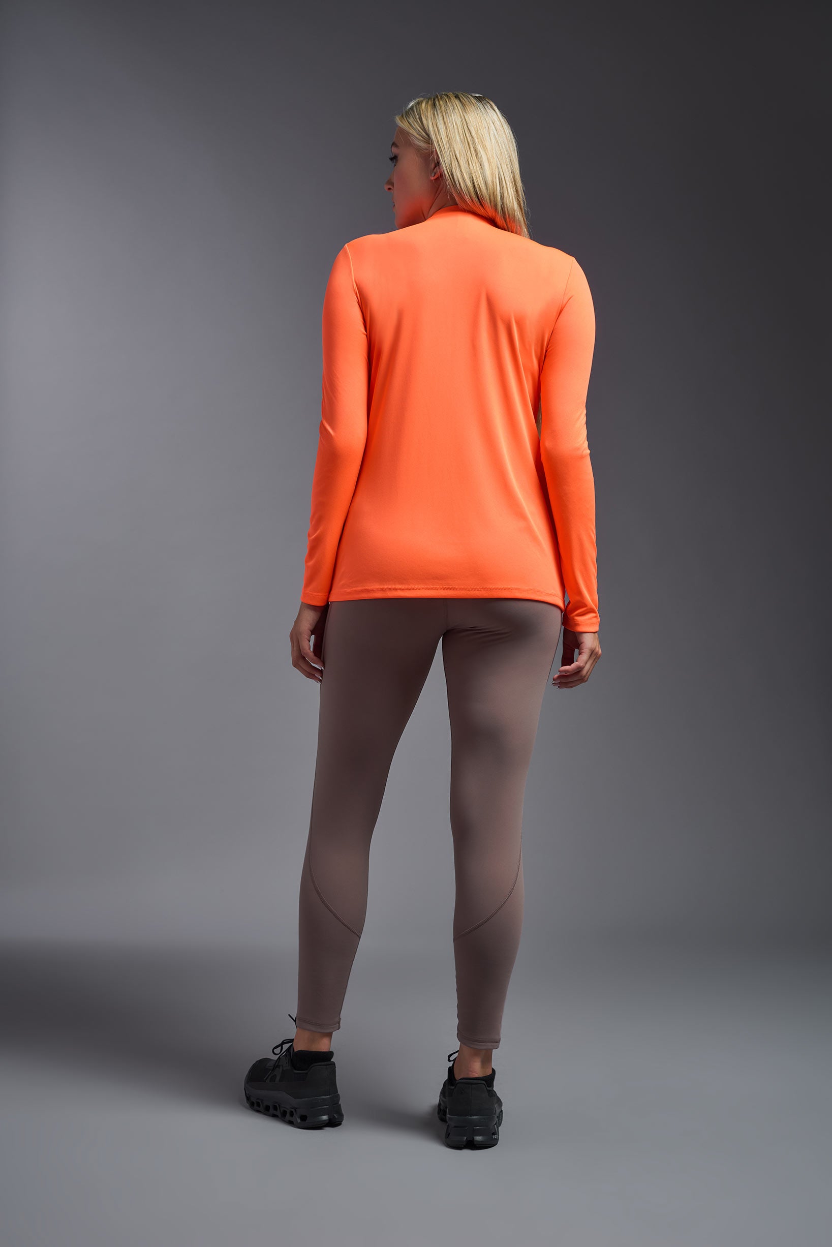 A female model wearing the women's DriMax V-Neck Long Sleeve Expert Tee  in the color safety orange, made out of 100% polyester, showing the relaxed fit from a back view. This shirt is quick-drying, moisture-wicking, with up to 30 UV protection and made in the USA. #safety-orange