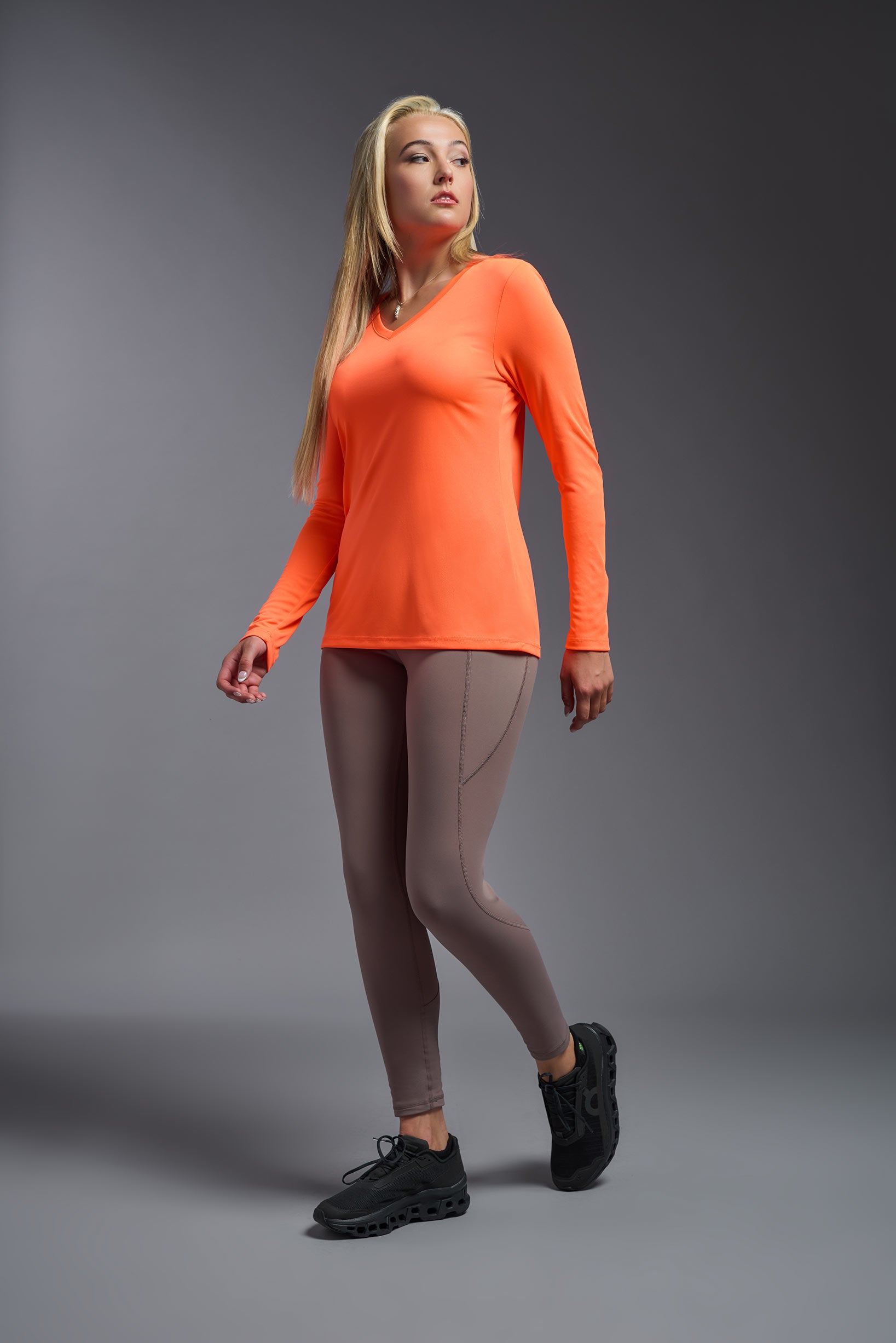 A female model wearing the women's DriMax V-Neck Long Sleeve Expert Tee  in the color safety orange, made out of 100% polyester, showing the relaxed fit from a side view. This shirt is quick-drying, moisture-wicking, with up to 30 UV protection and made in the USA. #safety-orange