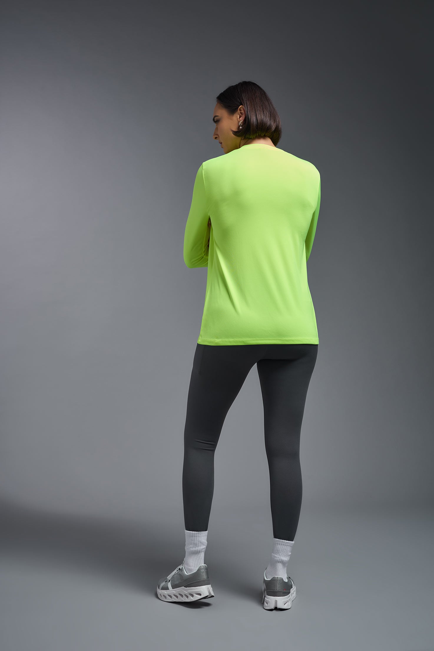A female model wearing the women's DriMax V-Neck Long Sleeve Expert Tee  in the color safety yellow, made out of 100% polyester, showing the relaxed fit from a back view. This shirt is quick-drying, moisture-wicking, with up to 30 UV protection and made in the USA. #safety-yellow