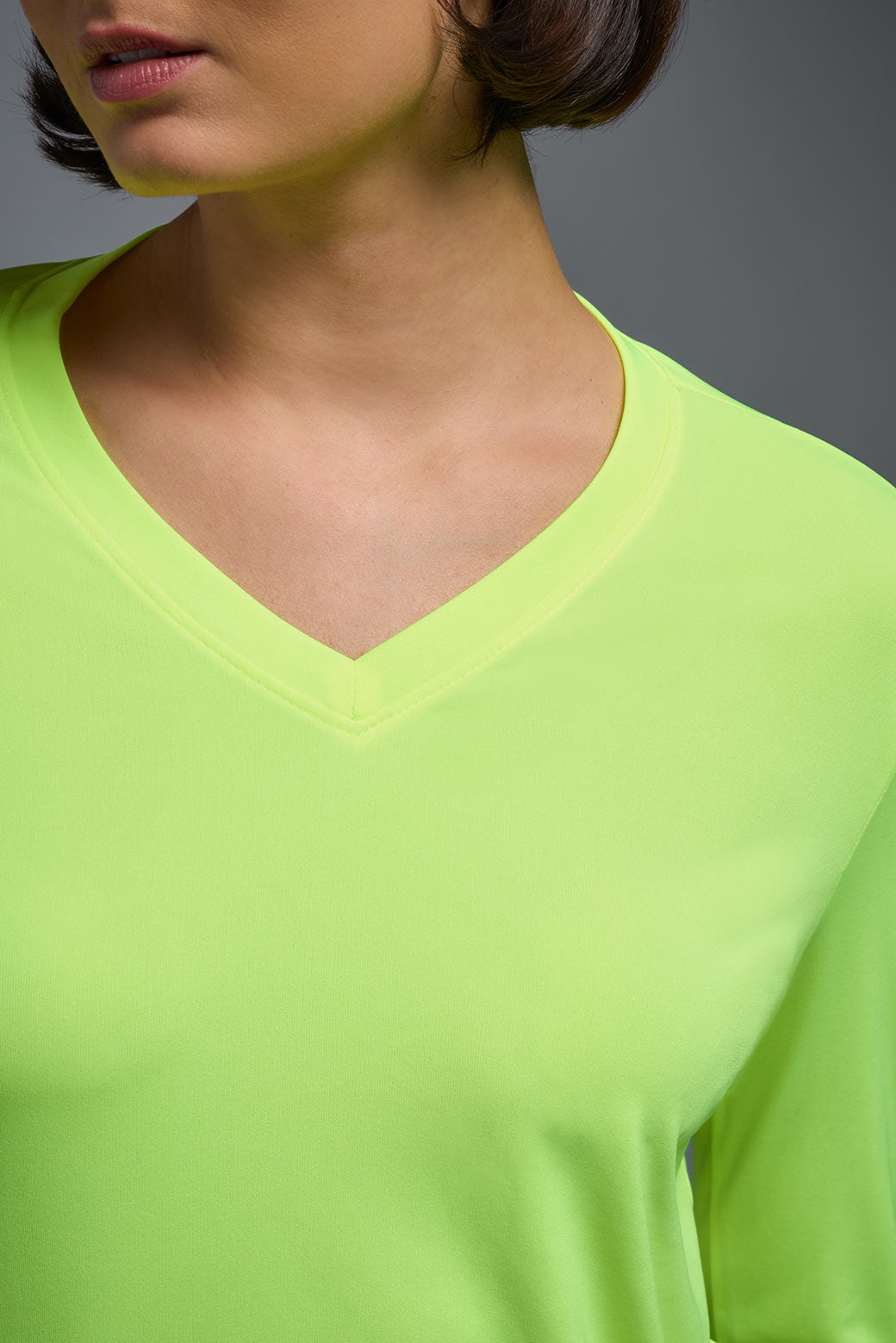 A female model wearing the women's DriMax V-Neck Long Sleeve Expert Tee  in the color safety yellow, made out of 100% polyester, showing the relaxed fit from a close-up collar view. This shirt is quick-drying, moisture-wicking, with up to 30 UV protection and made in the USA. #safety-yellow