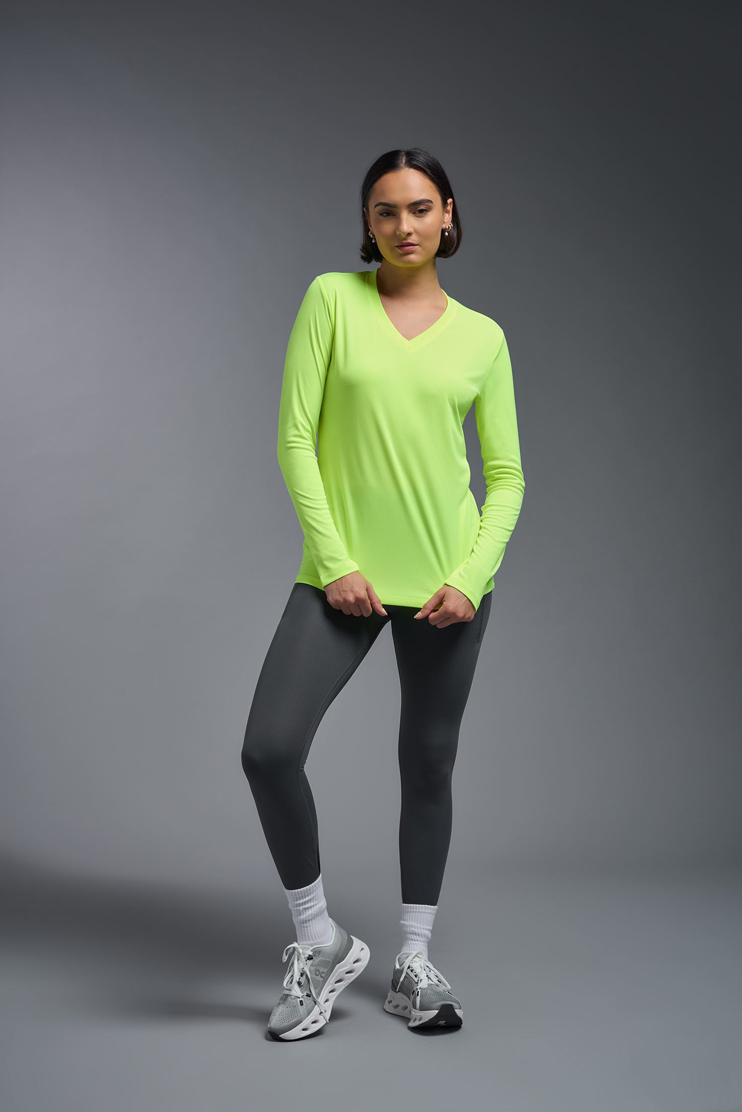A female model wearing the women's DriMax V-Neck Long Sleeve Expert Tee  in the color safety yellow, made out of 100% polyester, showing the relaxed fit from a front view. This shirt is quick-drying, moisture-wicking, with up to 30 UV protection and made in the USA. #safety-yellow