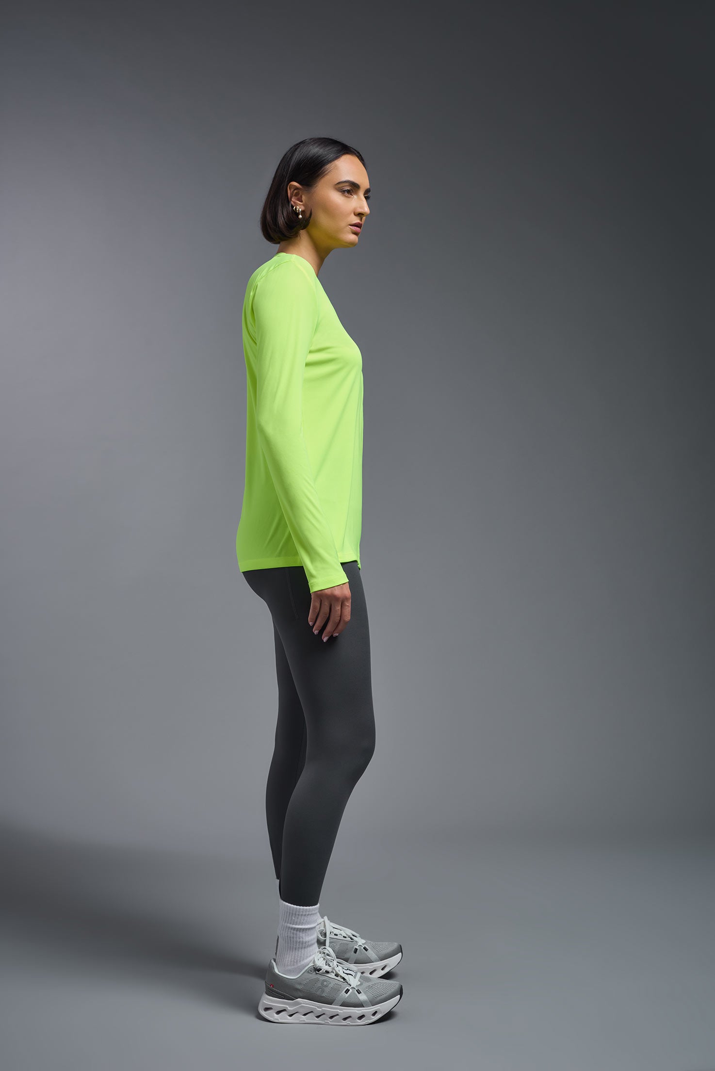 A female model wearing the women's DriMax V-Neck Long Sleeve Expert Tee  in the color safety yellow, made out of 100% polyester, showing the relaxed fit from a side view. This shirt is quick-drying, moisture-wicking, with up to 30 UV protection and made in the USA. #safety-yellow