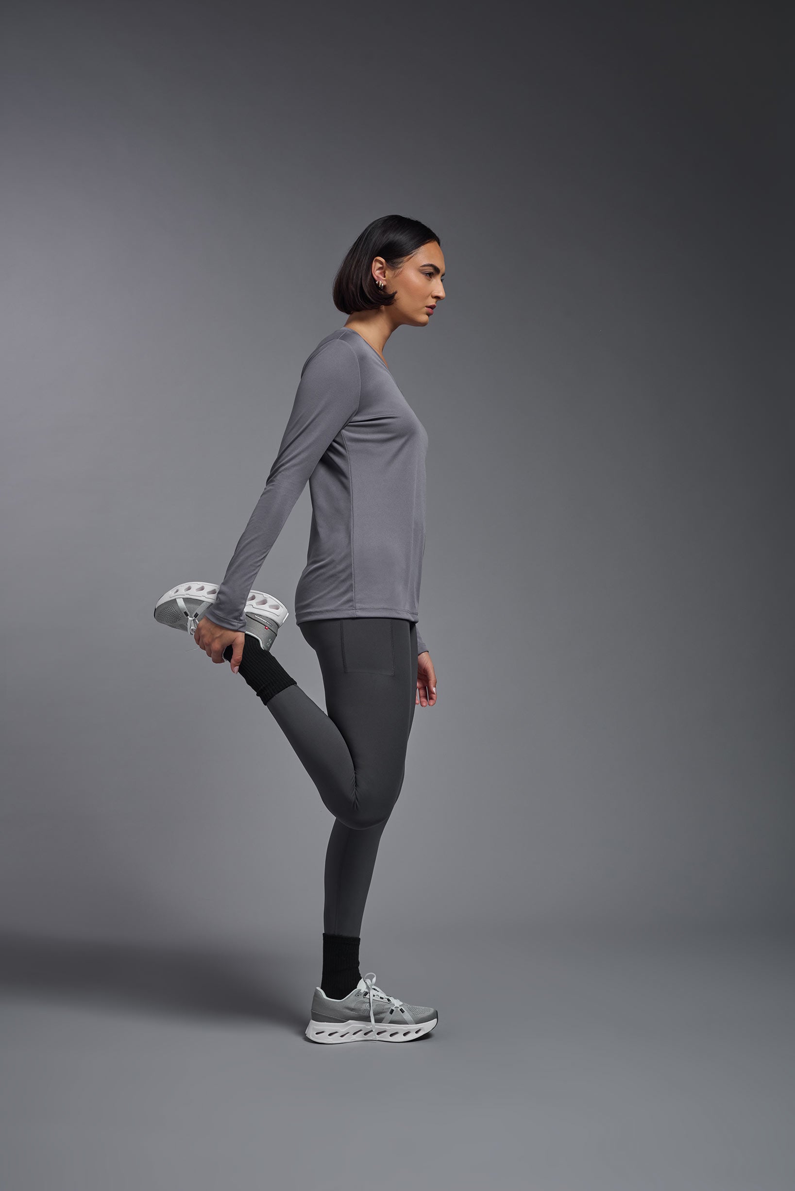 A female model wearing the women's DriMax V-Neck Long Sleeve Expert Tee  in the color steel gray, made out of 100% polyester, showing the relaxed fit from a side view. This shirt is quick-drying, moisture-wicking, with up to 30 UV protection and made in the USA. #steel