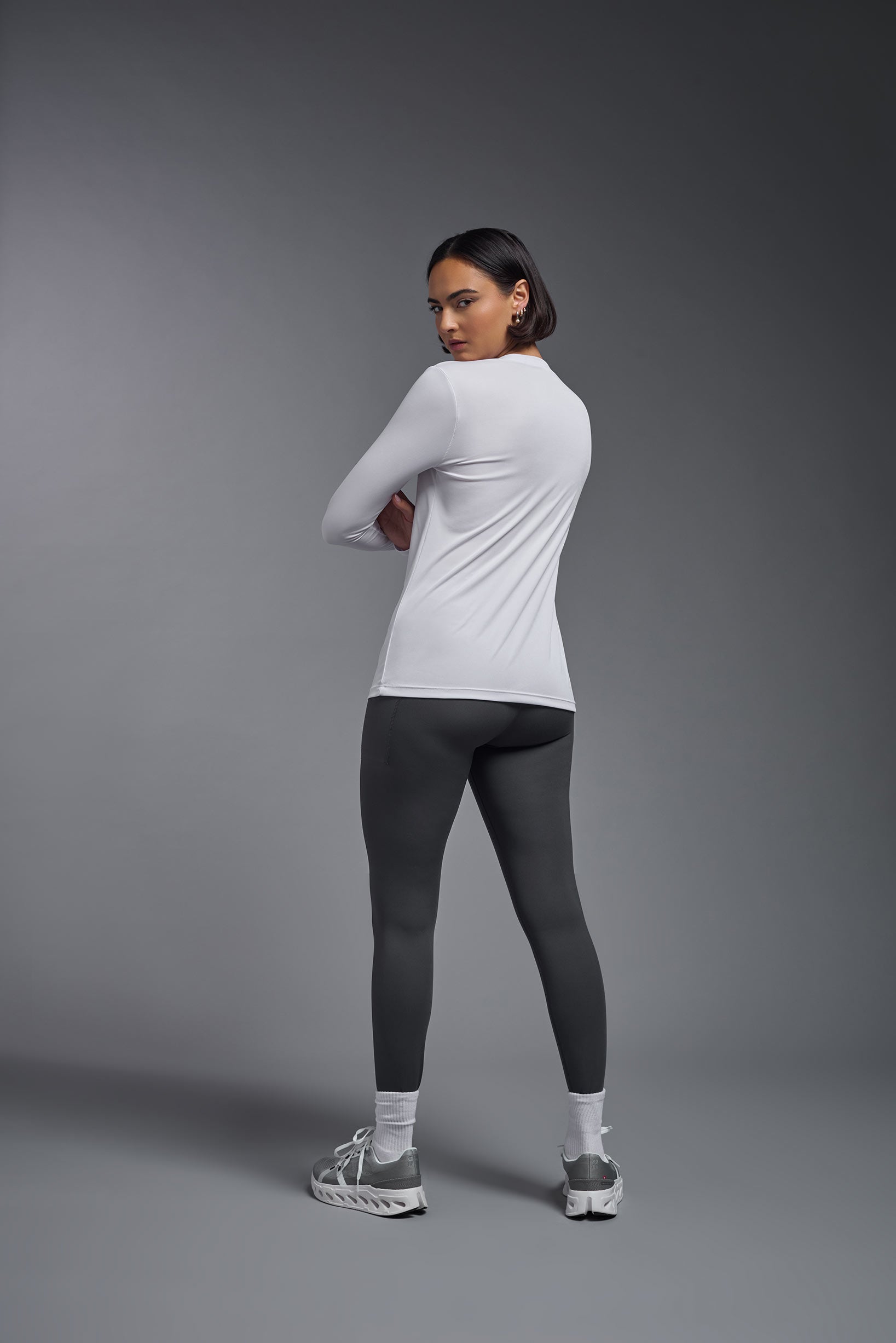 A female model wearing the women's DriMax V-Neck Long Sleeve Expert Tee  in the color white, made out of 100% polyester, showing the relaxed fit from a back view. This shirt is quick-drying, moisture-wicking, with up to 30 UV protection and made in the USA. #white