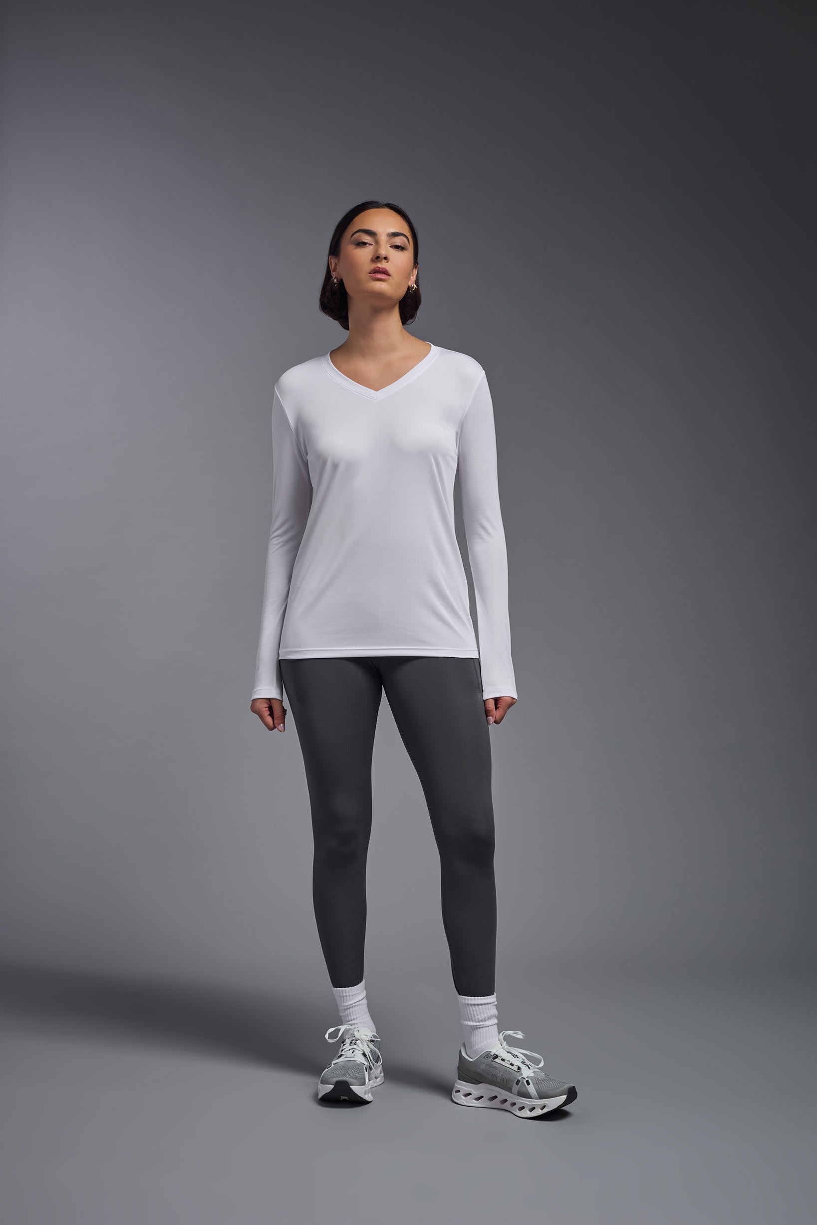 A female model wearing the women's DriMax V-Neck Long Sleeve Expert Tee  in the color white, made out of 100% polyester, showing the relaxed fit from a front view. This shirt is quick-drying, moisture-wicking, with up to 30 UV protection and made in the USA. #white