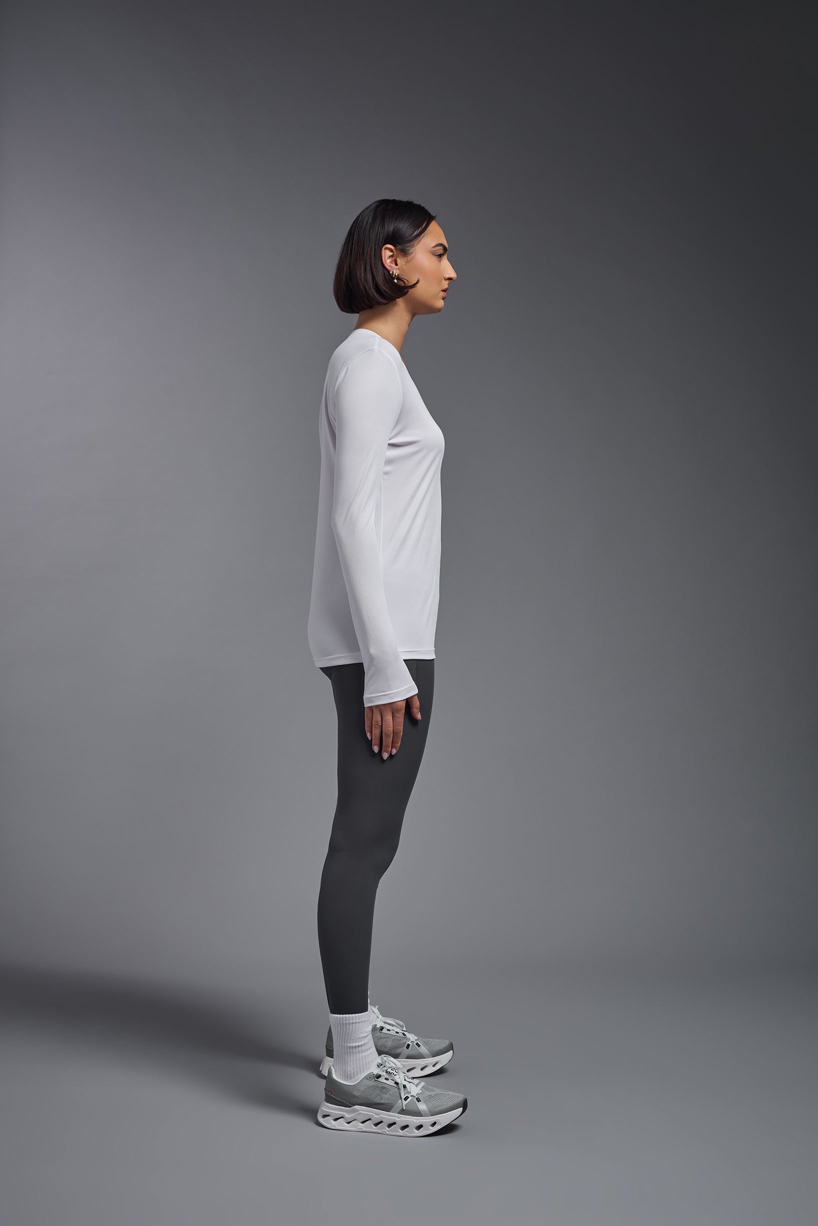 A female model wearing the women's DriMax V-Neck Long Sleeve Expert Tee  in the color white, made out of 100% polyester, showing the relaxed fit from a side view. This shirt is quick-drying, moisture-wicking, with up to 30 UV protection and made in the USA. #white