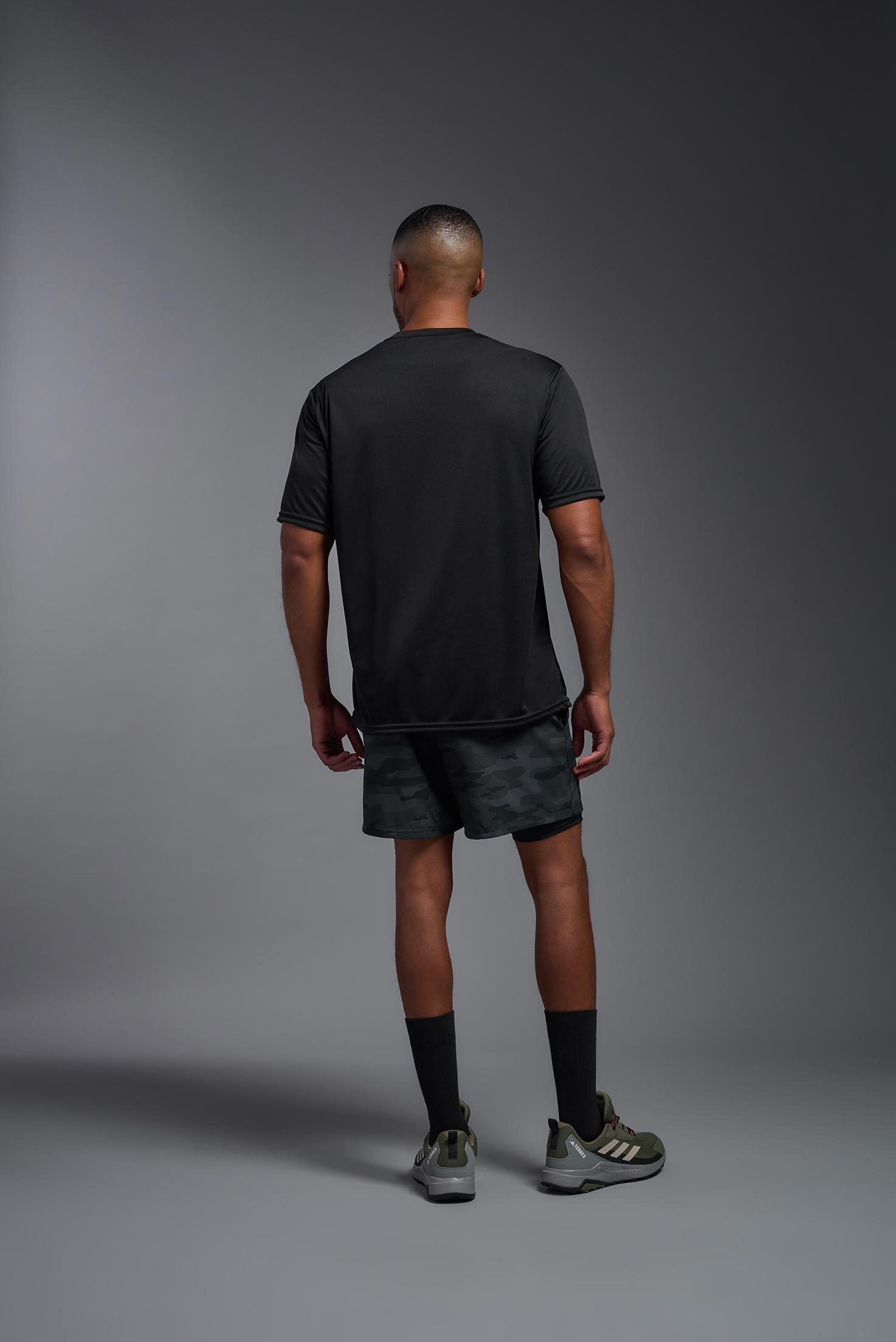 A male model wearing the men's DriMax Expert Tee in the color black, made out of 100% polyester, showing the relaxed fit from a back view. This shirt is moisture-wicking, quick-drying, and made in the USA. #black