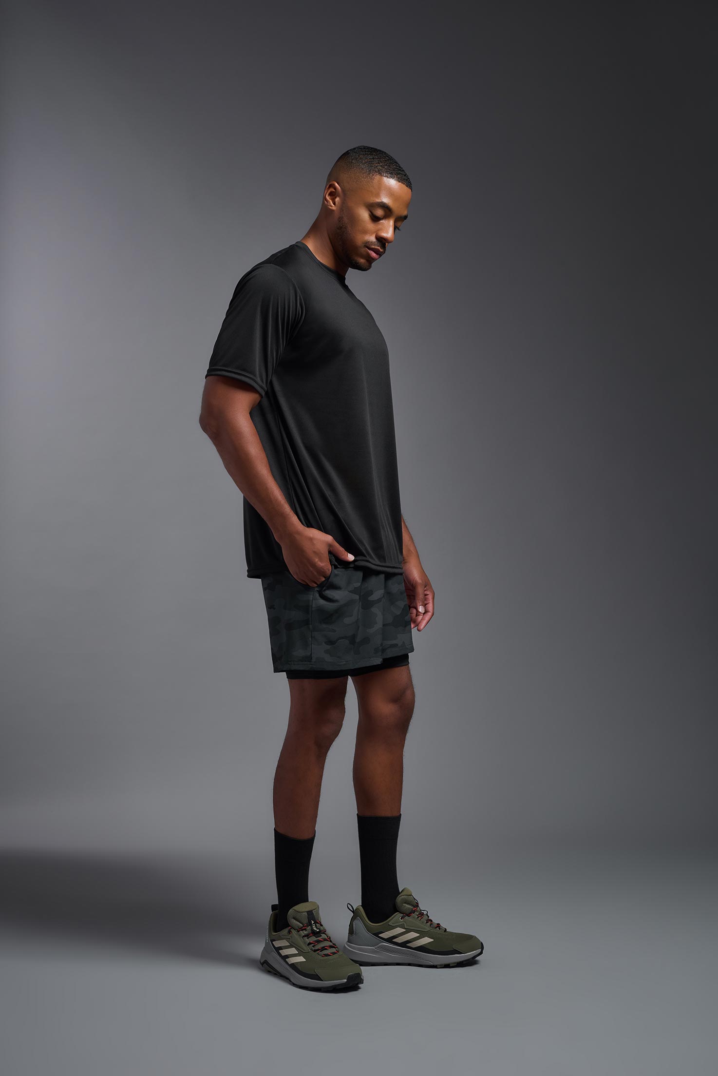 A male model wearing the men's DriMax Expert Tee in the color black, made out of 100% polyester, showing the relaxed fit from a side view. This shirt is moisture-wicking, quick-drying, and made in the USA. #black