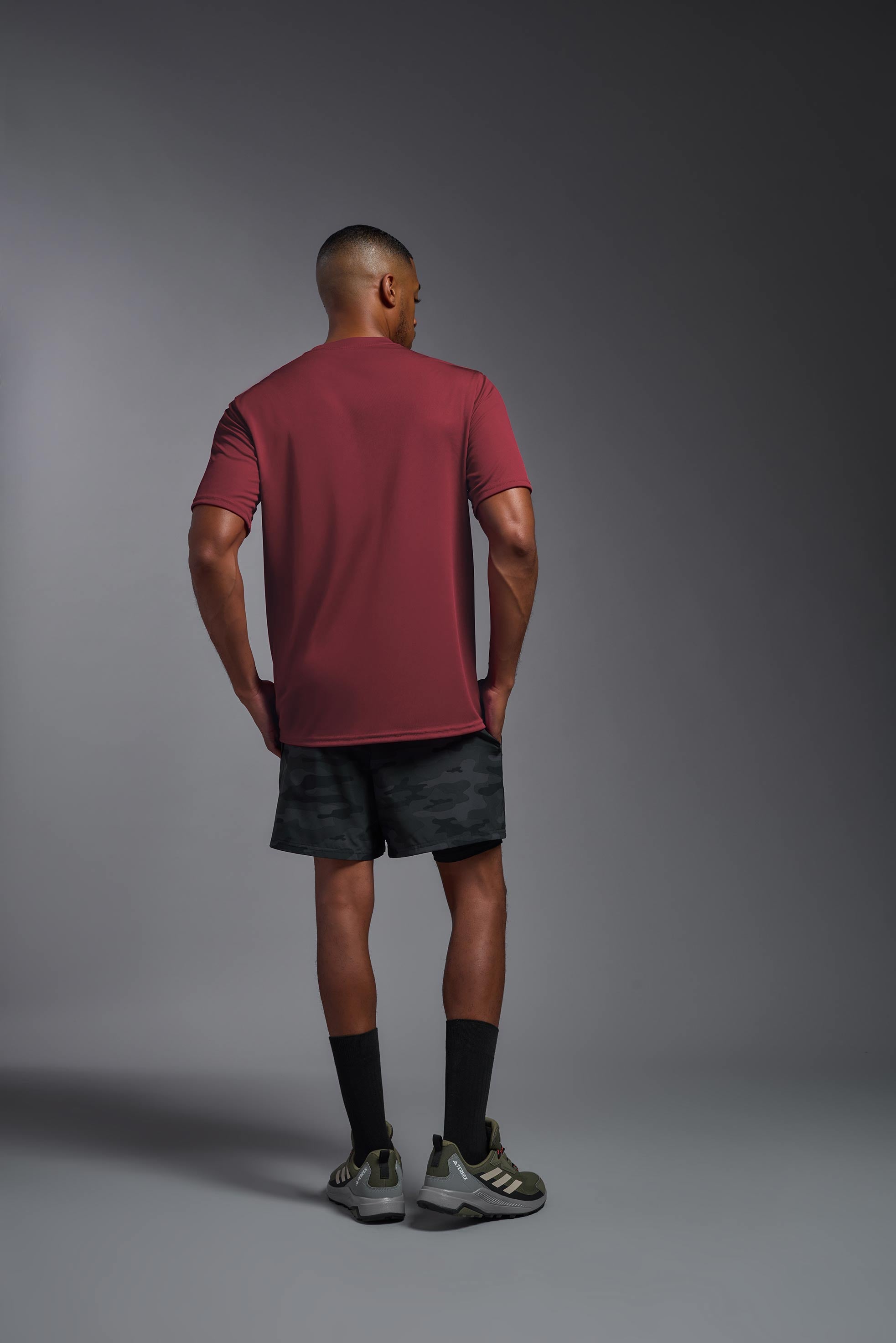 A male model wearing the men's DriMax Expert Tee in the color cardinal, made out of 100% polyester, showing the relaxed fit from a back view. This shirt is quick-drying, moisture-wicking, and made in the USA. #cardinal