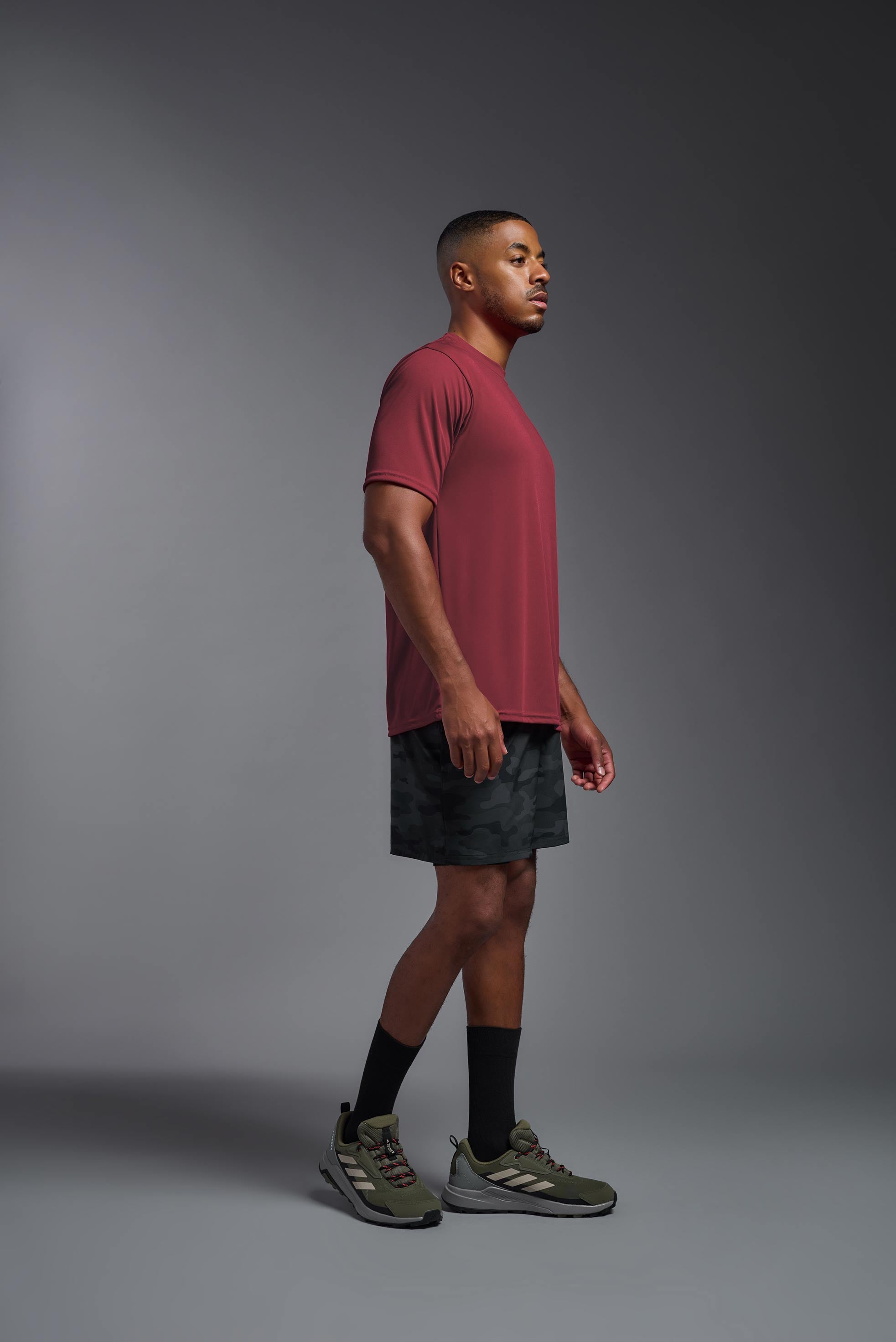 A male model wearing the men's DriMax Expert Tee in the color cardinal, made out of 100% polyester, showing the relaxed fit from a side view. This shirt is quick-drying, moisture-wicking, and made in the USA. #cardinal