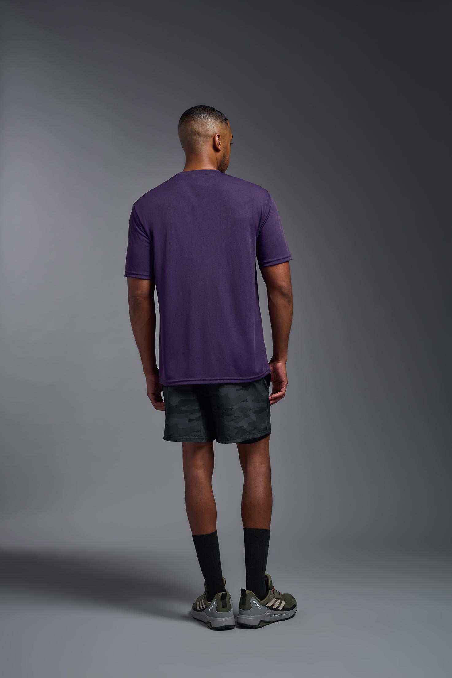 A male model wearing the men's DriMax Expert Tee in the color dark purple, made out of 100% polyester, showing the relaxed fit from a back view. This shirt is moisture-wicking, quick-drying, and made in the USA. #deep-purple