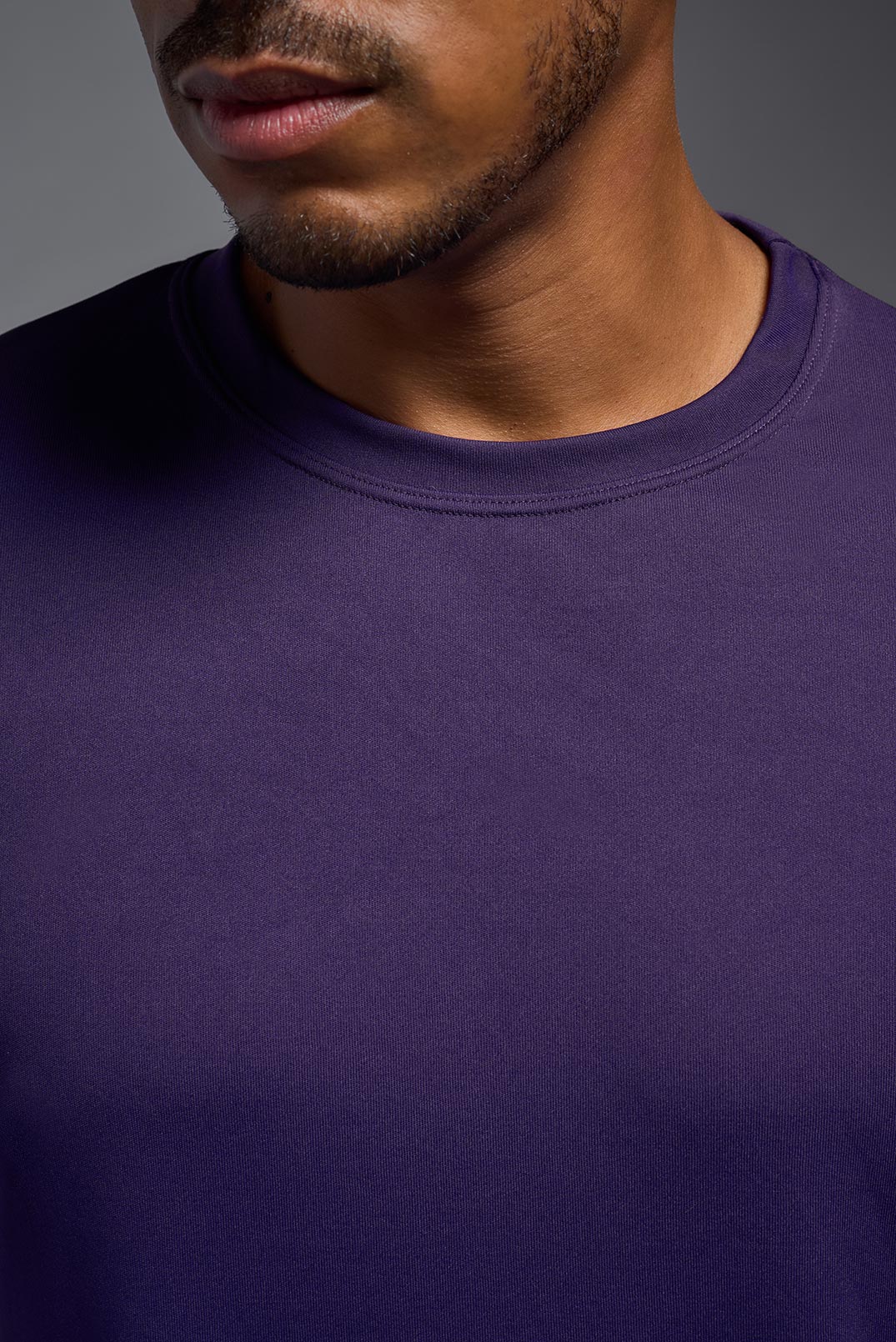 A male model wearing the men's DriMax Expert Tee in the color dark purple, made out of 100% polyester, showing the relaxed fit from a close-up collar view. This shirt is moisture-wicking, quick-drying, and made in the USA. #deep-purple
