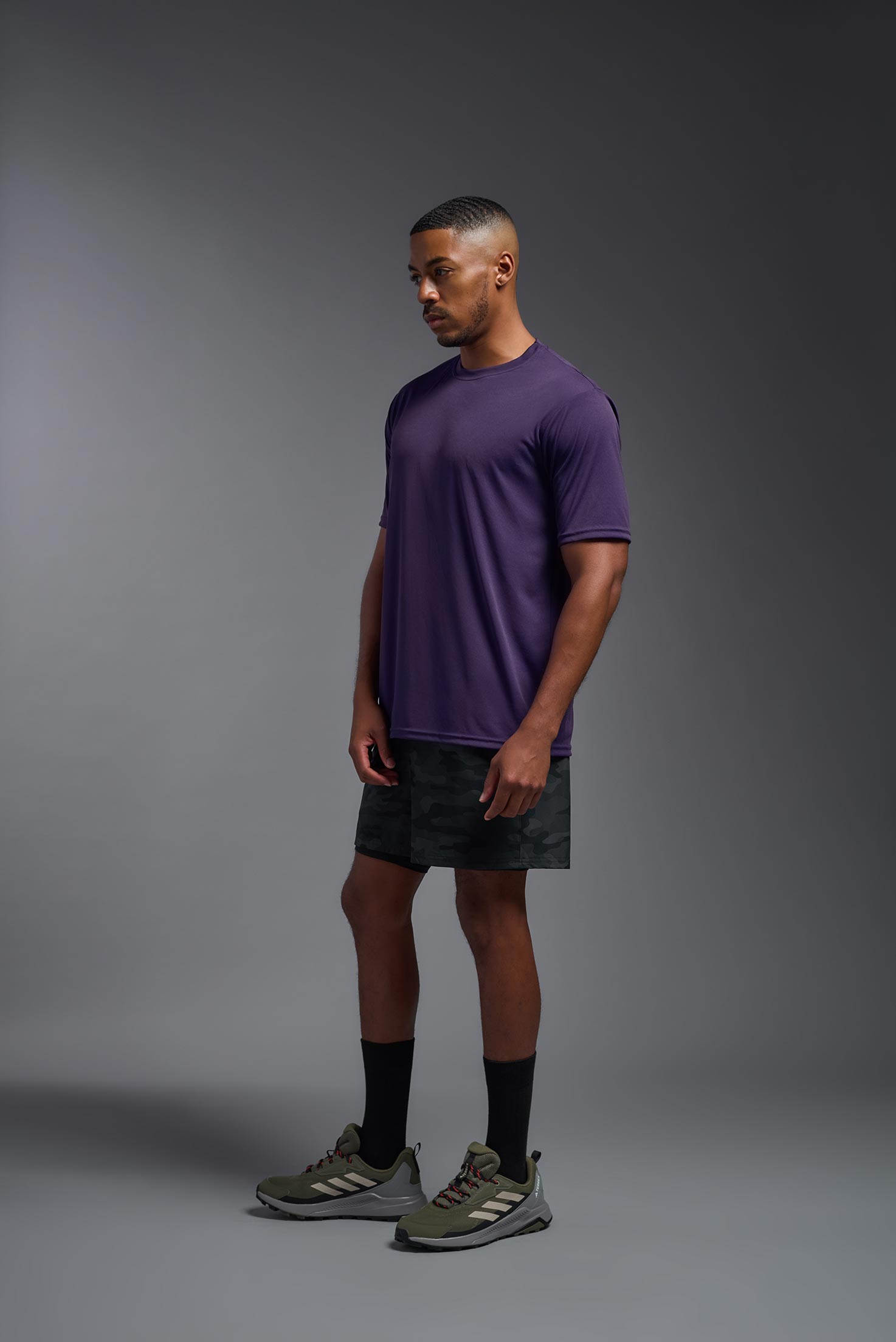 A male model wearing the men's DriMax Expert Tee in the color dark purple, made out of 100% polyester, showing the relaxed fit from a side view. This shirt is moisture-wicking, quick-drying, and made in the USA. #deep-purple