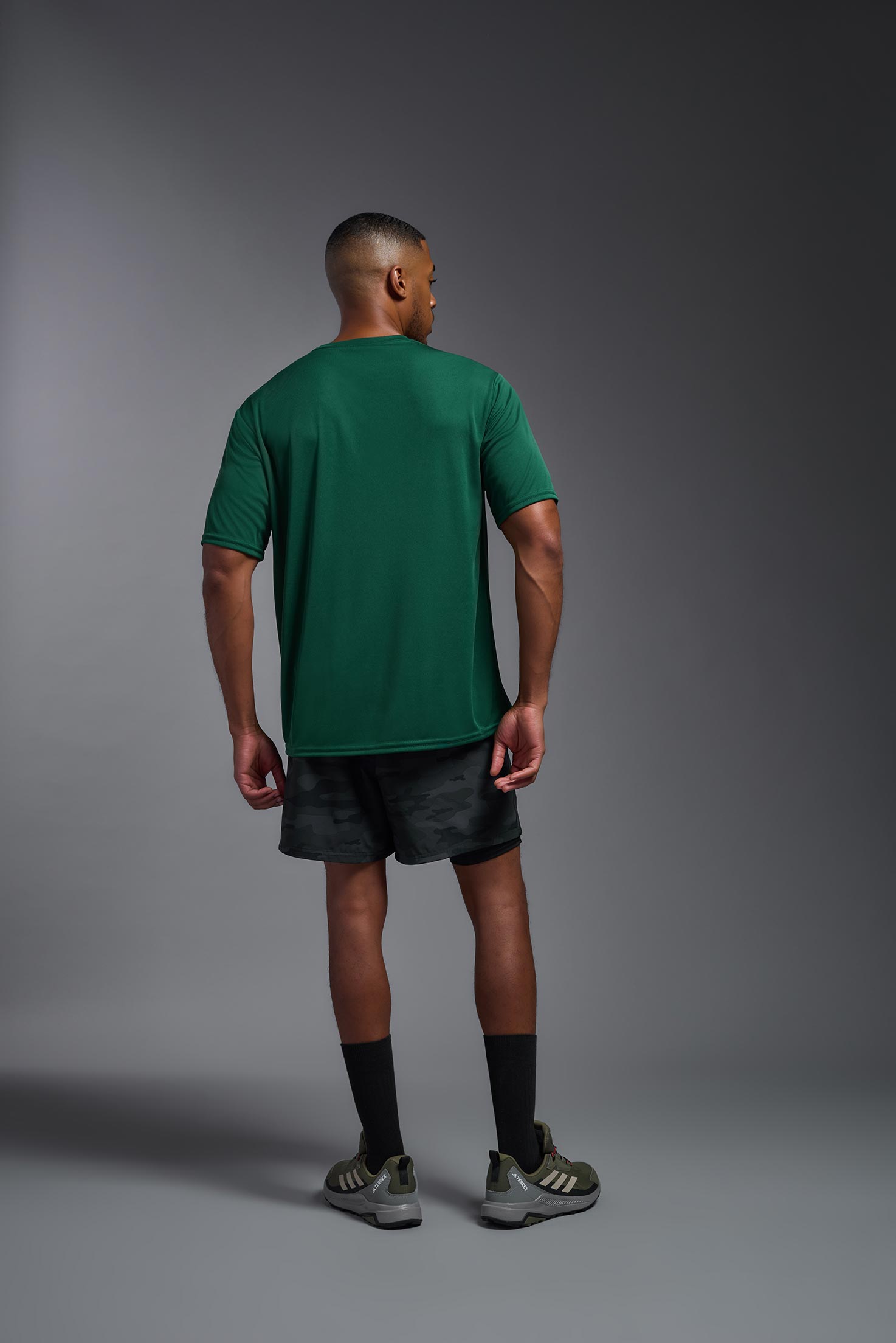 A male model wearing the men's DriMax Expert Tee in forest green, made out of 100% polyester, showing the relaxed fit from a back view. This shirt is moisture-wicking, quick-drying, and made in the USA. #forest-green