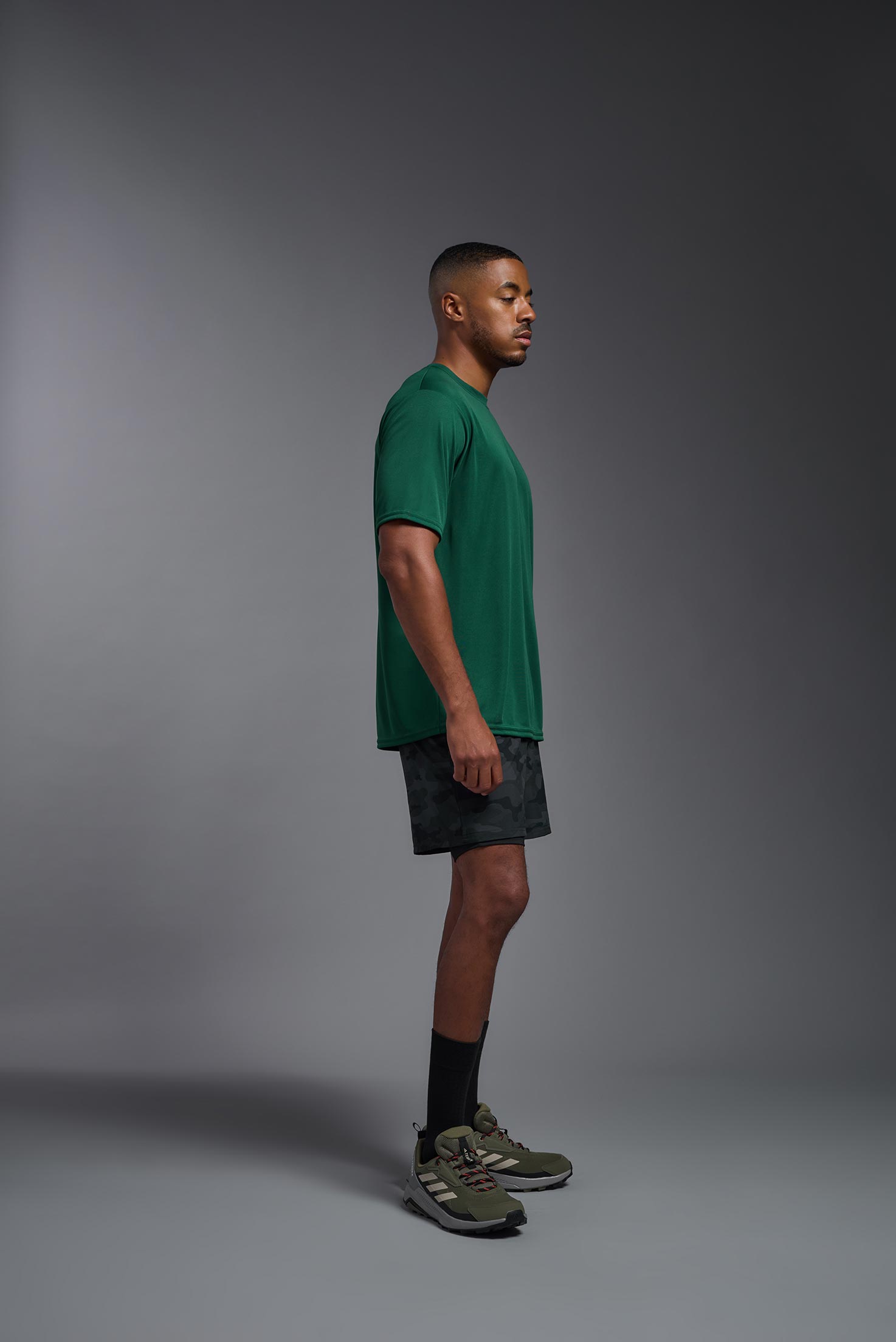 A male model wearing the men's DriMax Expert Tee in forest green, made out of 100% polyester, showing the relaxed fit from a side view. This shirt is moisture-wicking, quick-drying, and made in the USA. #forest-green