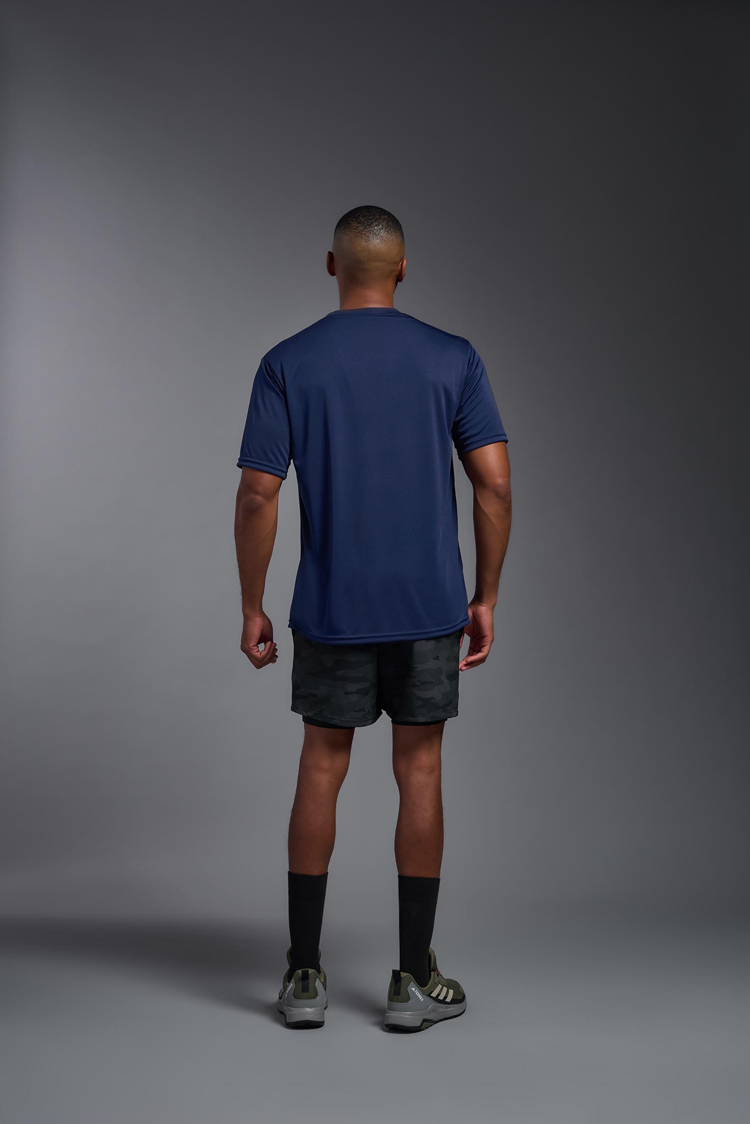 A male model wearing the men's DriMax Expert Tee in the color navy, made out of 100% polyester, showing the relaxed fit from a back view. #navy