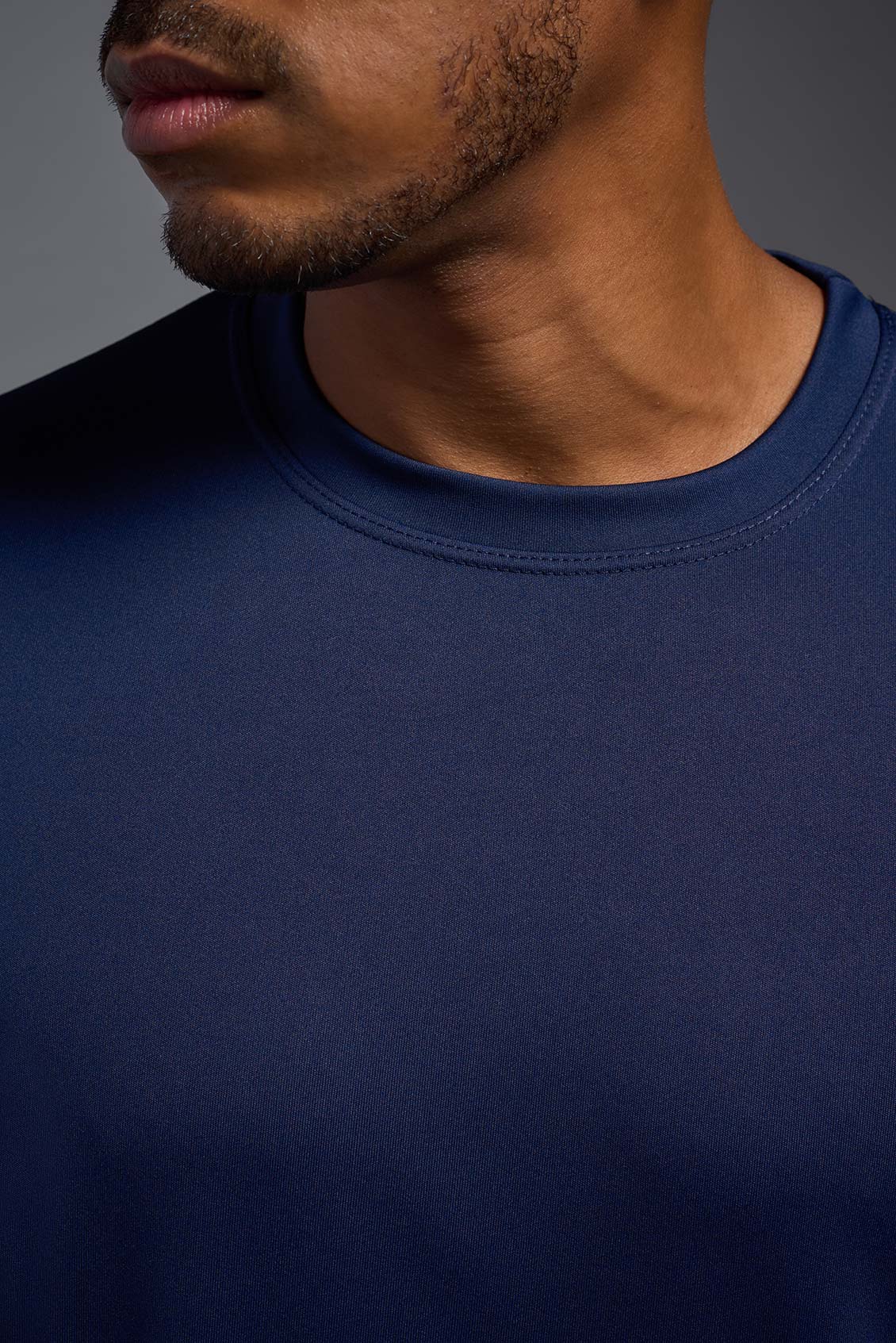 A male model wearing the men's DriMax Expert Tee in the color navy, made out of 100% polyester, showing the relaxed fit from a collar close-up view. #navy