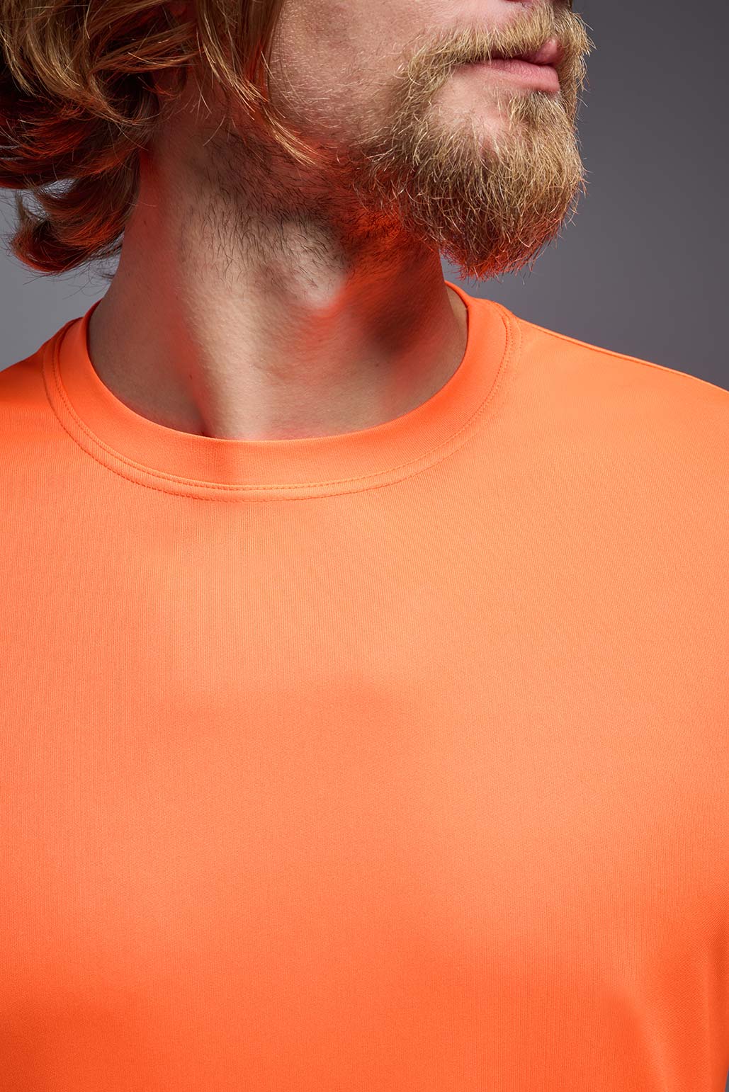 A male model wearing the men's DriMax Expert Tee in safety orange, made out of 100% polyester, showing the relaxed fit from a front detail collar view. #safety-orange