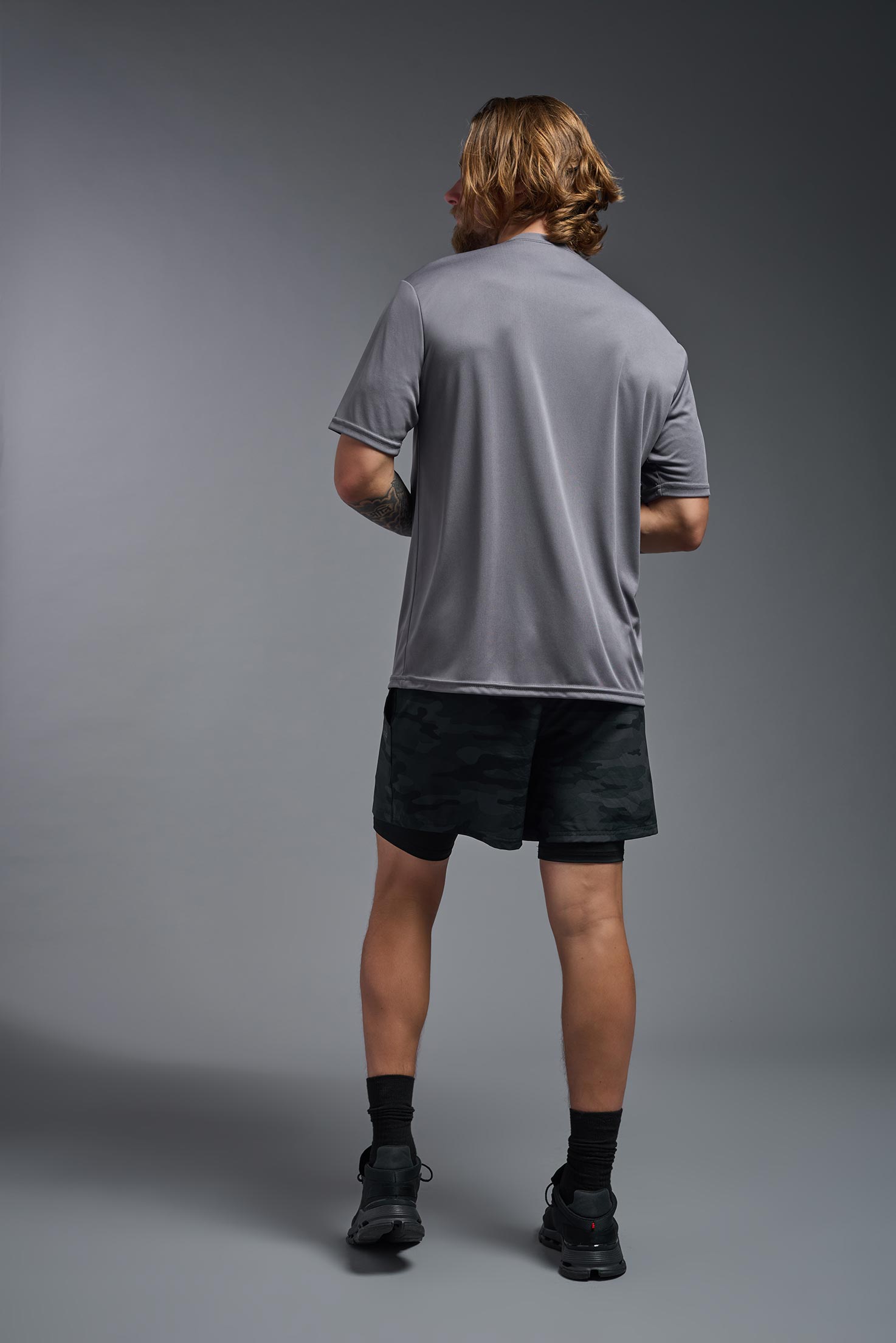 A male model wearing the men's DriMax Expert Tee in the color steel, made out of 100% polyester, showing the relaxed fit from a back view. This shirt is moisture-wicking, quick-drying, and made in the USA. #steel