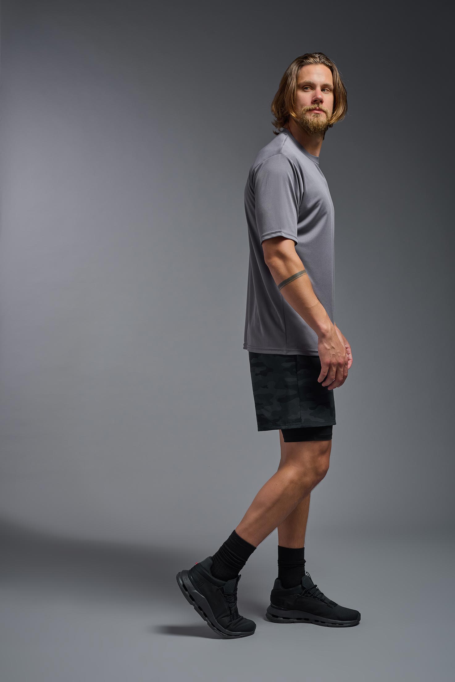 A male model wearing the men's DriMax Expert Tee in the color steel, made out of 100% polyester, showing the relaxed fit from a side view. This shirt is moisture-wicking, quick-drying, and made in the USA. #steel