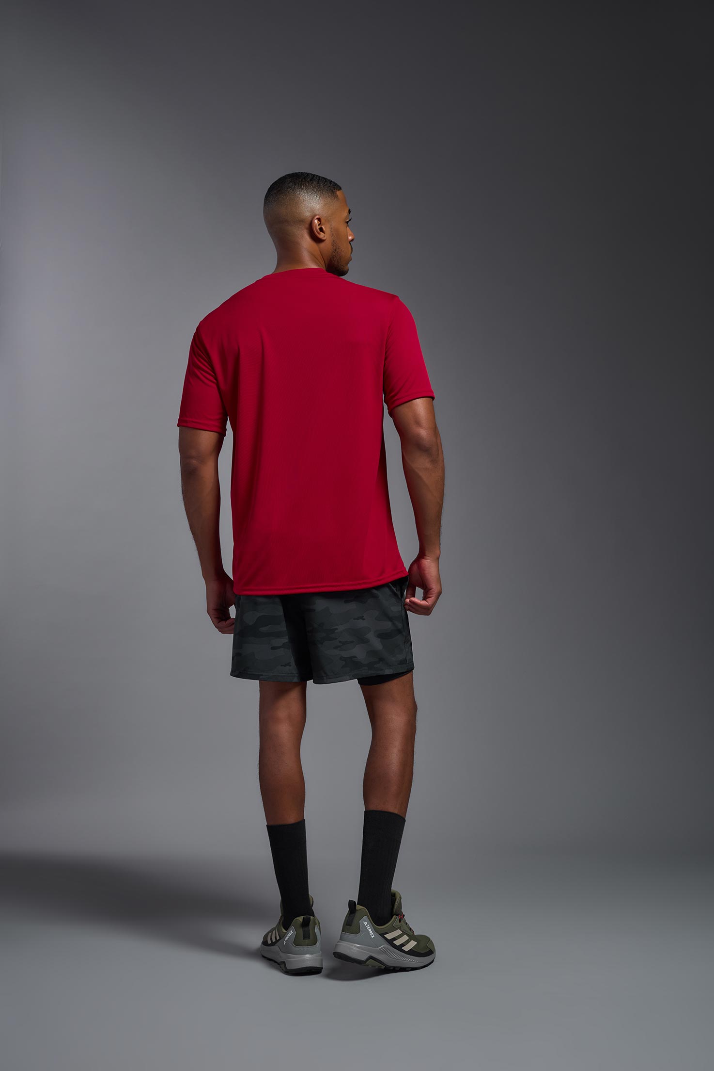 A male model wearing the men's DriMax Expert Tee in the color red, made out of 100% polyester, showing the relaxed fit from a back view. This shirt is moisture-wicking, quick-drying, and made in the USA. #red