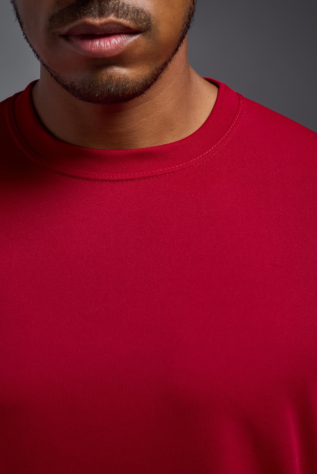 A male model wearing the men's DriMax Expert Tee in the color red, made out of 100% polyester, showing the relaxed fit from a front collar detail view. #red