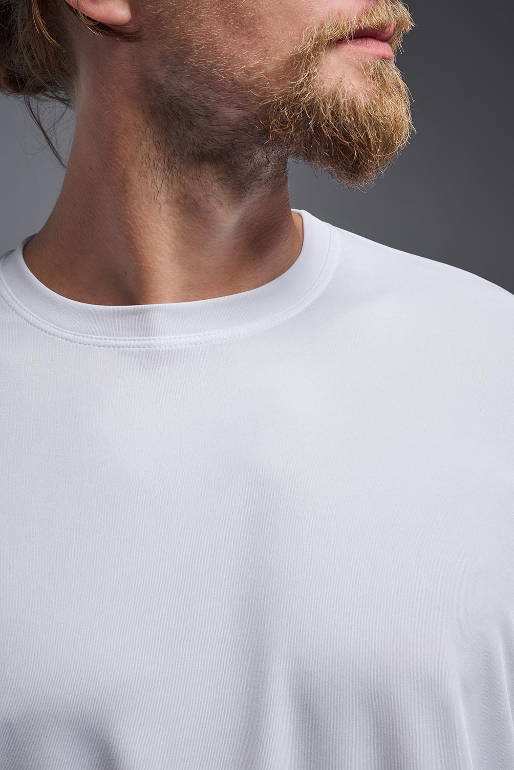 A male model wearing the men's DriMax Expert Tee in the color white, made out of 100% polyester, showing the relaxed fit from a collar close-up view. #white