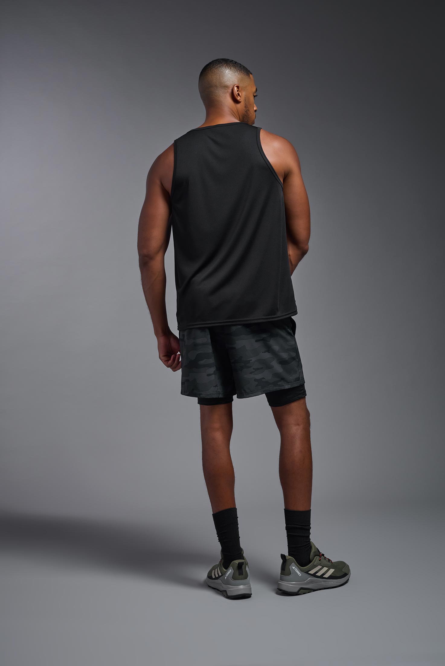 A male model wearing the men's DriMax Endurance Tank in the color black, made out of 100% polyester, showing the relaxed fit from a back view. #black