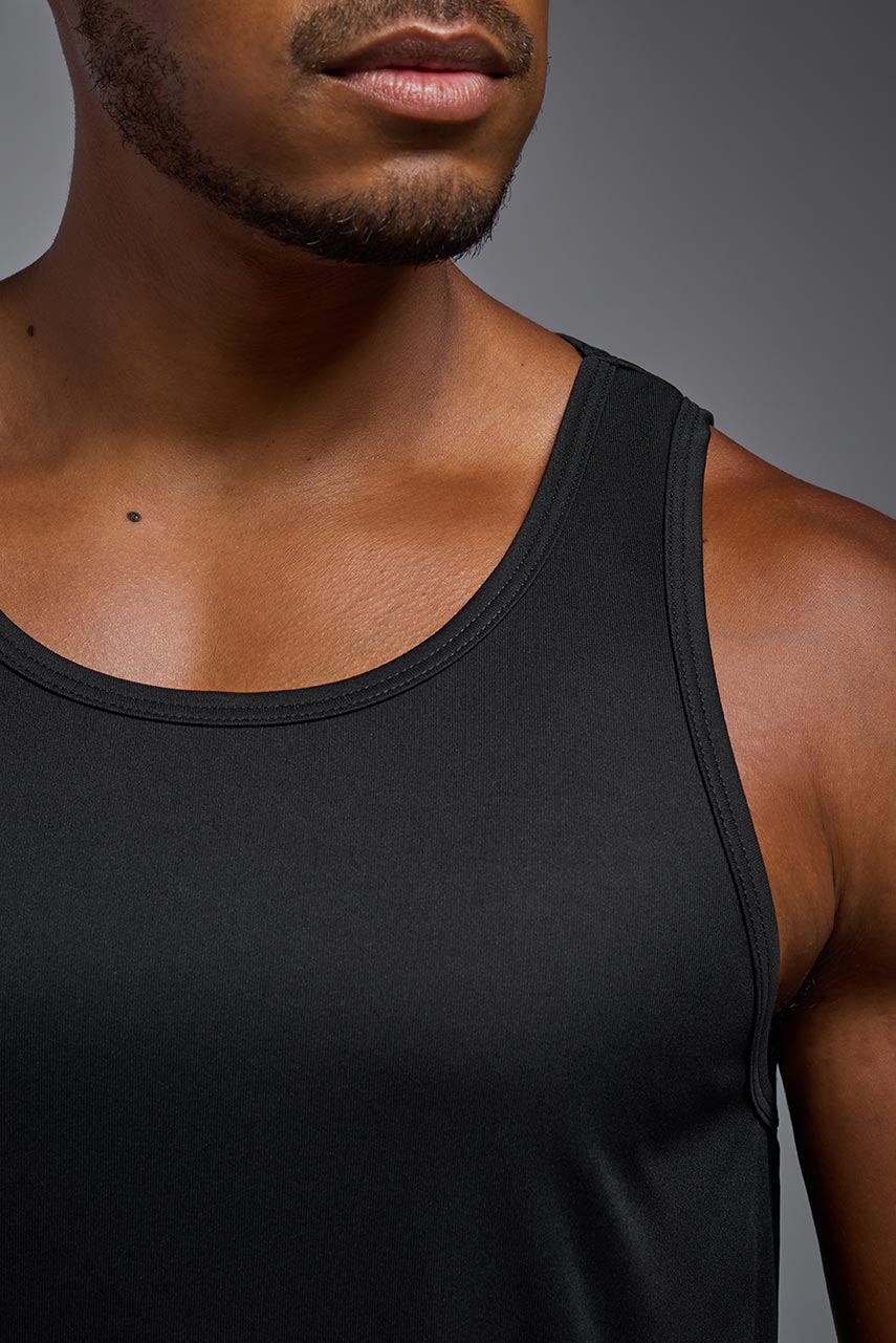 A male model wearing the men's DriMax Endurance Tank in the color black, made out of 100% polyester, showing the relaxed fit from a close-up detail view. #black