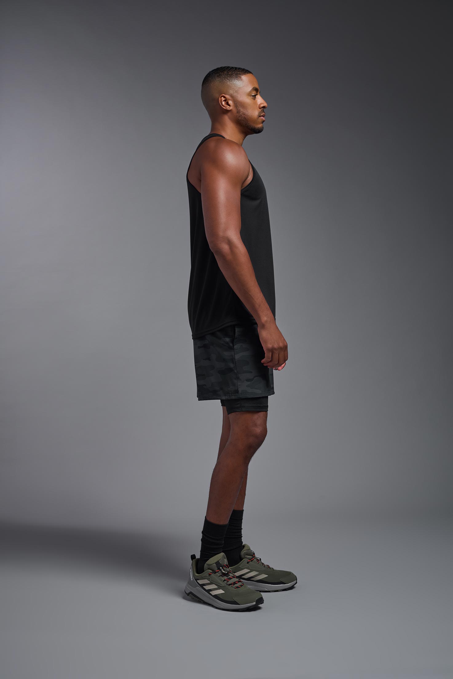A male model wearing the men's DriMax Endurance Tank in the color black, made out of 100% polyester, showing the relaxed fit from a side view. #black