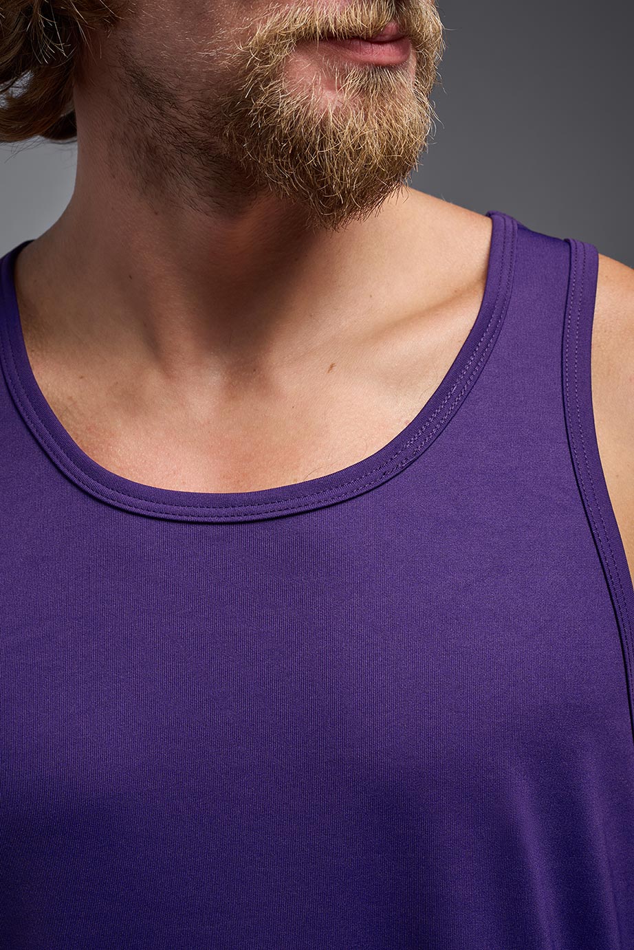 A male model wearing the men's DriMax Endurance Tank in the color deep purple, made out of 100% polyester, showing the relaxed fit from a close up collar view. #deep-purple